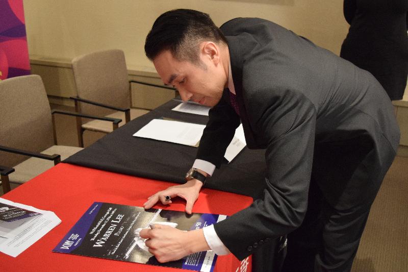 Pianist Warren Lee today (November 9, New York time) autographs his concert poster at the press conference.