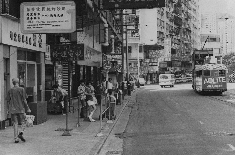 「沿途風光好：1970年代香港島巴士站街景照片展」的其中一幀圖片：一九七五年的英皇道街頭景貌及行駛中的電車拖卡。