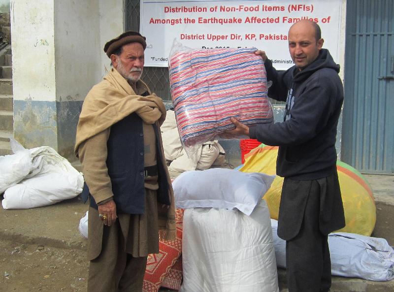 Local staff of the relief organisation pass household items, such as kitchenware, buckets, mattresses, pillows, blankets and shawls, to earthquake victims in Pakistan.