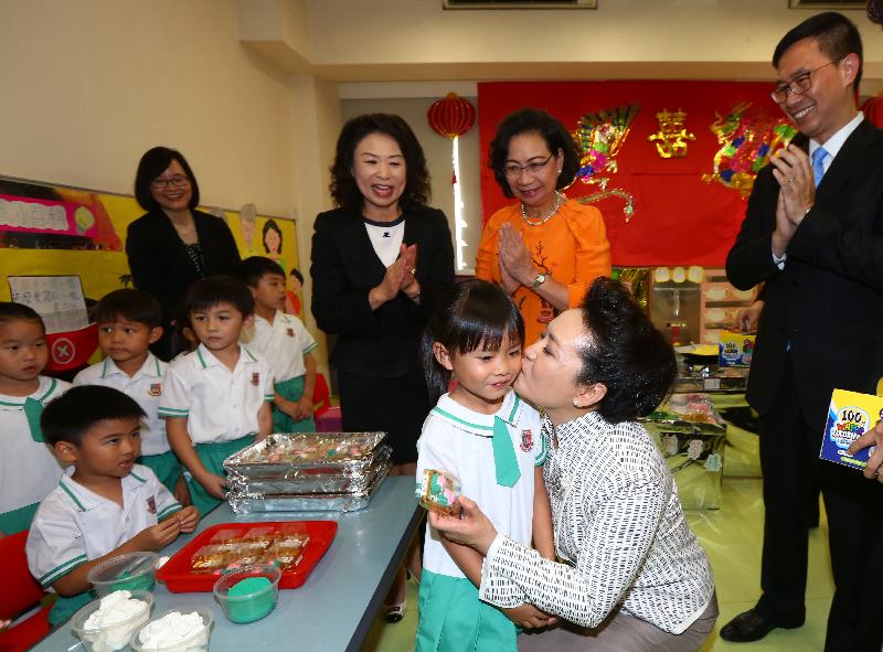 The wife of President Xi Jinping, Peng Liyuan (front, right), kissing a girl who had just presented a souvenir to her. Looking on are the wife of the Chief Executive, Mrs Regina Leung (back row, second right); the Under Secretary for Education, Mr Kevin Yeung (back row, first right); and the kindergarten's principal, Ms Lee Ming-chu (back row, third right).