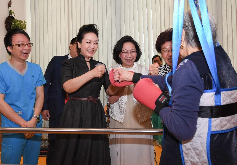 The wife of President Xi Jinping, Peng Liyuan (second left), gives encouragement to an elderly person receiving therapeutic training during her visit at TWGHs Jockey Club Sunshine Complex for the Elderly in Wong Chuk Hang this morning (June 30). Looking on are the wife of the Chief Executive, Mrs Regina Leung (third left); and Deputy Director of the Liaison Office of the Central People's Government in the Hong Kong Special Administrative Region Ms Yin Xiaojing (fourth left).