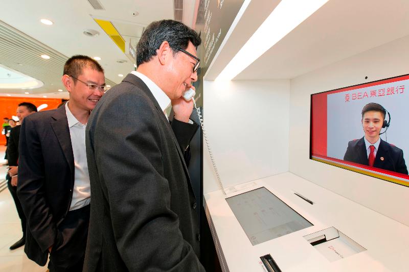 東亞銀行執行董事兼副行政總裁李民橋（左）今日（八月十七日）在天水圍向香港金融管理局總裁陳德霖（右）介紹視像櫃員機。