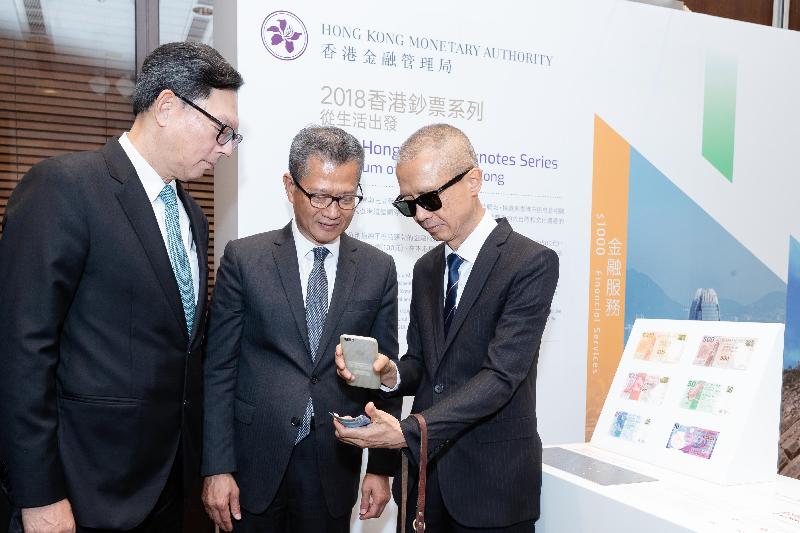 財政司司長陳茂波（中）及香港金融管理局總裁陳德霖（左）觀看如何使用手機應用程式『讀鈔易』辨認香港鈔票的面額。