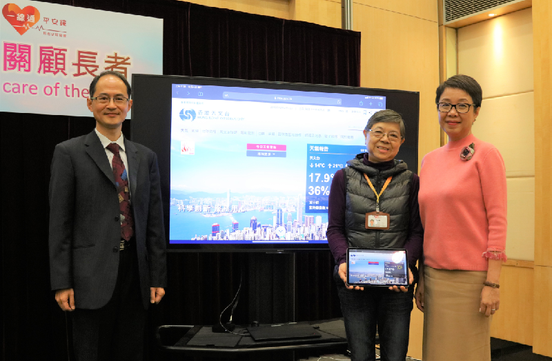 香港天文台助理台长郑楚明博士（左一）和长者安居协会行政总裁王虹虹（右一）于联合记者会后与长者安居协会的义工合照。图片的背景为天文台刚于上月底推出全新面貌的网站。