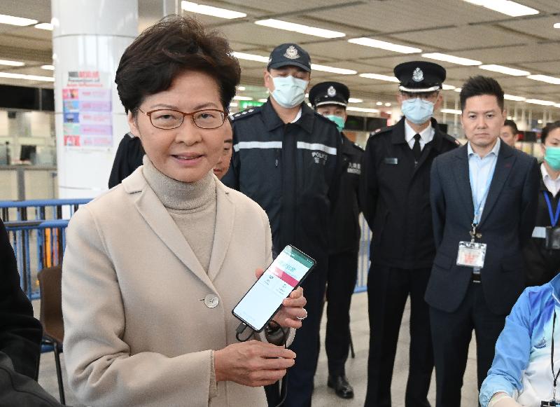 林郑月娥（左一）在深圳湾口岸了解如何为须检疫人士佩戴电子手环，以监察他们有否留在居所。图示林郑月娥与配合电子手环使用的手机。