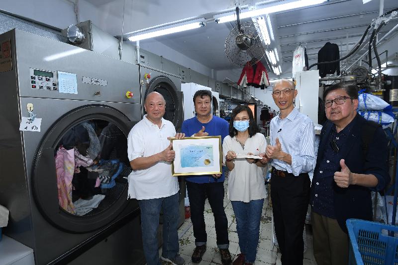 The Secretary for the Environment, Mr Wong Kam-sing (second right), today (June 18) visited a laundry workshop and a laundry shop, which are beneficiaries of the Anti-epidemic Subsidy Scheme for the Laundry Trade. The two shops have positively joined energy efficiency and carbon reduction initiatives. Picture shows the operators of the laundry shop holding their local renewable energy certificate.

