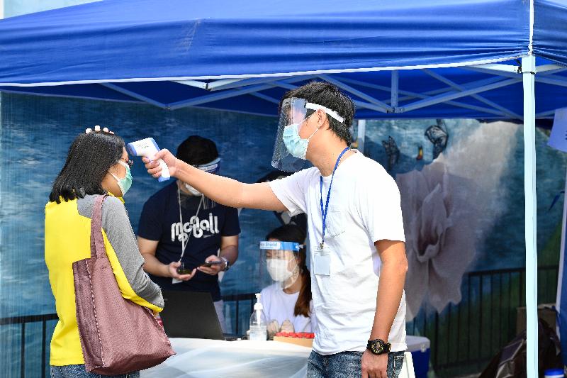 In order to identify cases in the community as early as possible to help cut transmission chains, the Government has arranged a testing agency to provide free specimen collection and COVID-19 testing services through mobile specimen collection stations in Tai Po for three consecutive days starting today (November 9). Photo shows a testing agency staff member checking the body temperature of a member of the public at the open space outside Fu Shin Community Hall.
