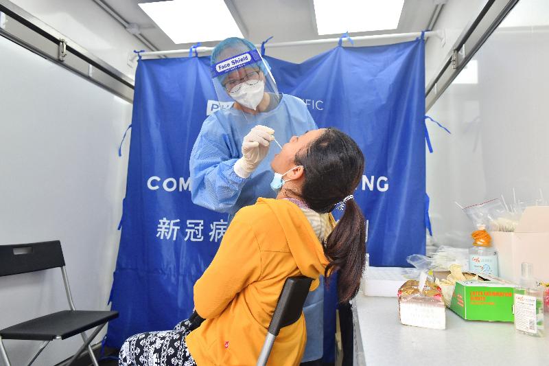 The Labour Department (LD) set up mobile specimen collection stations at popular gathering places of foreign domestic helpers (FDHs) to provide a free COVID-19 testing service for FDHs today (March 14). Photo shows a staff member of the testing agent collecting a specimen from an FDH at the mobile specimen collection station at Lai Chi Kok Park.