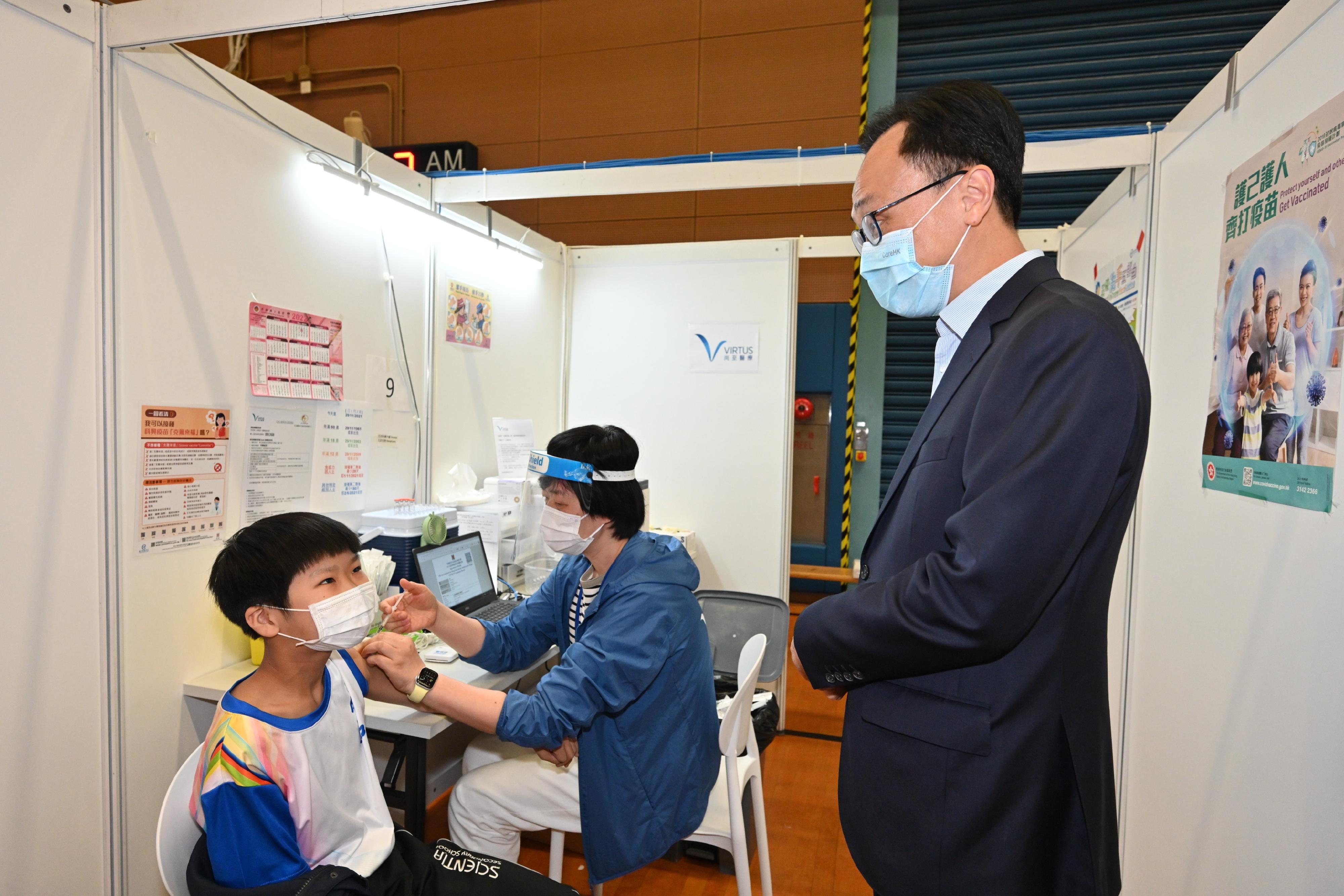 Persons aged between 12 and 17 have been able to receive the Sinovac vaccine since December 2. Scientia Secondary School is the first school to have students vaccinated with the Sinovac vaccine at a Community Vaccination Centre (CVC) through group booking. The Secretary for the Civil Service, Mr Patrick Nip, visited the CVC at Kwun Chung Sports Centre this afternoon (December 3) to view the administering of the vaccine to some 30 students of the school. Photo shows Mr Nip (right) chatting with a student receiving his COVID-19 vaccination.
