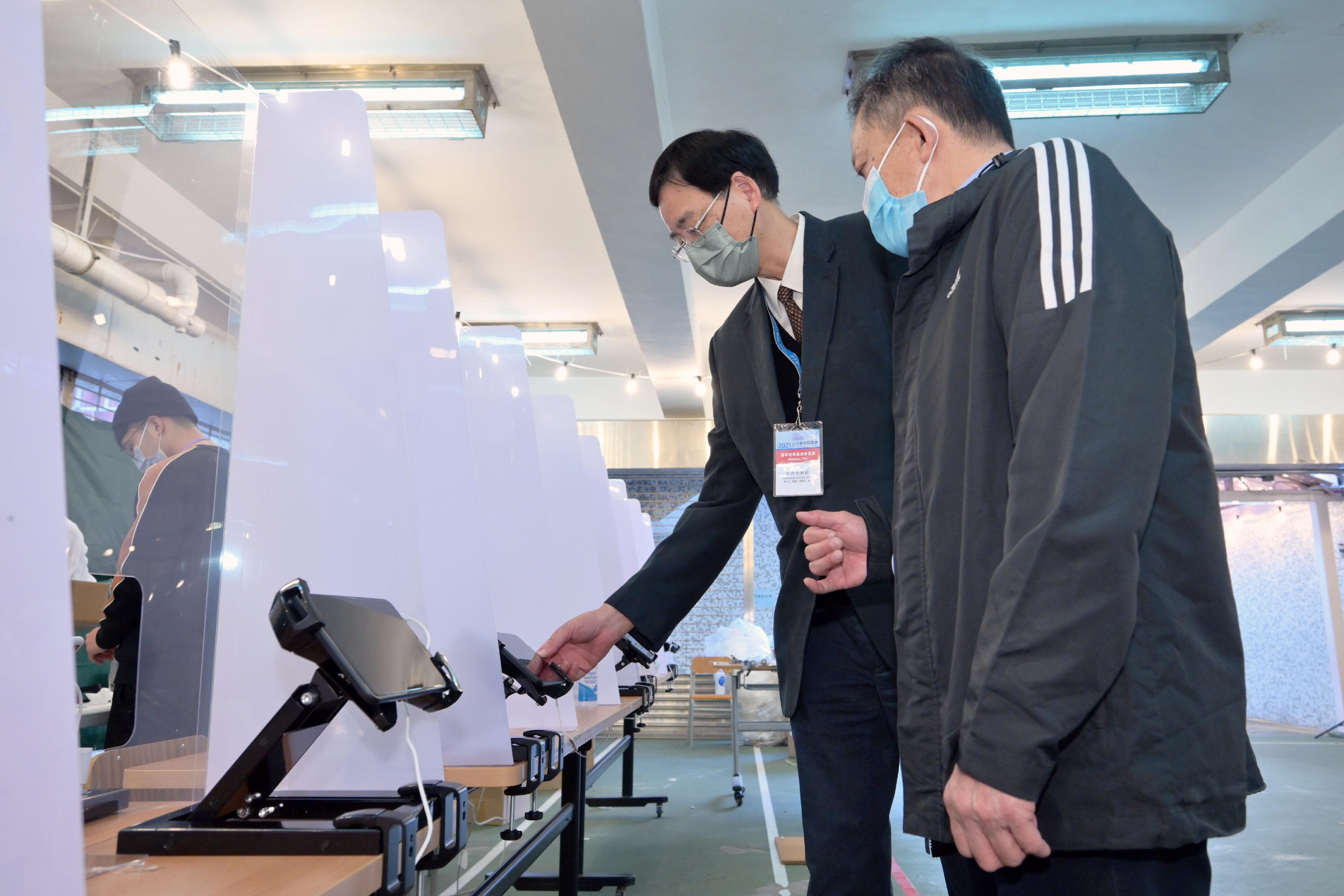 Electoral Affairs Commission member Professor Daniel Shek (left), visits the polling station of the 2021 Legislative Council General Election at Fung Kai Liu Yun Sum Memorial School today (December 18) to inspect the electoral preparation work. He is briefed by the Presiding Officer on the operation of the Electronic Poll Register system.