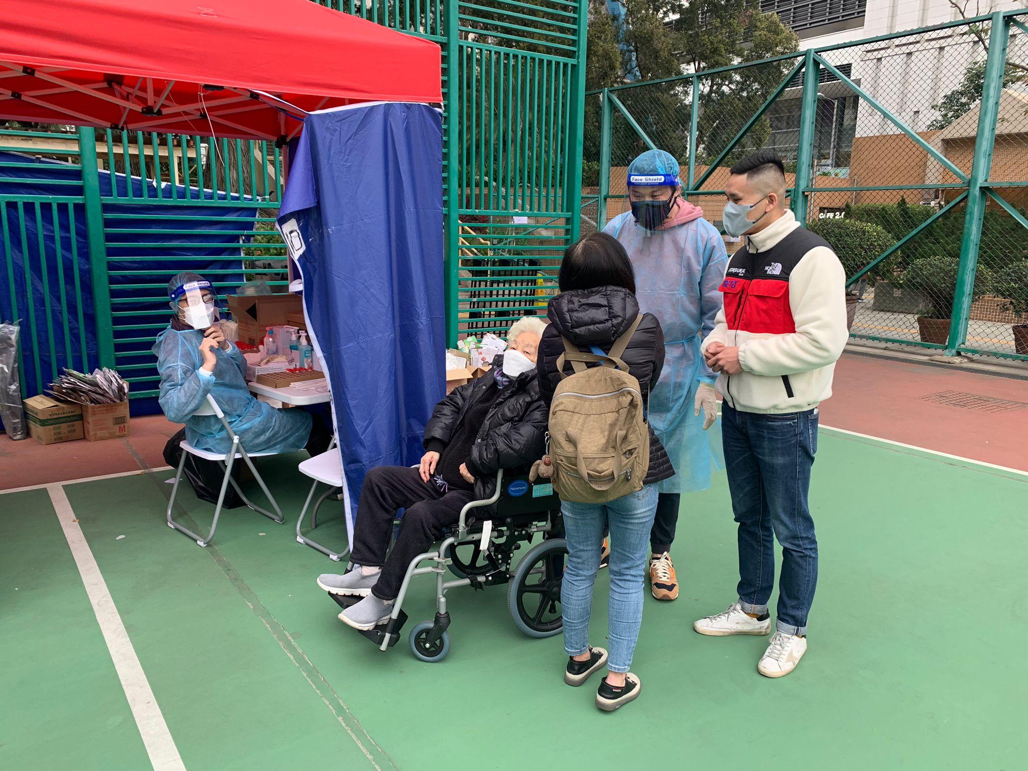 The District Officer (Wong Tai Sin), Mr Steve Wong (first right), together with a volunteer, arranged for priority specimen collection for an elderly citizen with ambulatory difficulty at Wong Tai Sin Muk Lun Street Playground mobile testing station today (February 10).