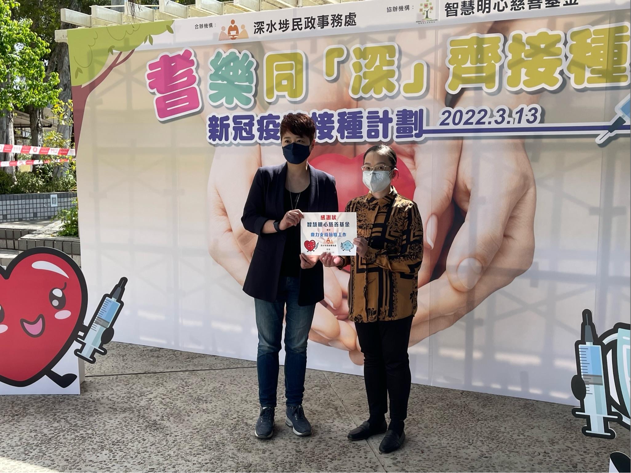 The Acting Director of Home Affairs, Miss Vega Wong, officiated at the launch ceremony of a community vaccination programme for the elderly named "Vaccination for the Elderly in SSP" organised by the Sham Shui Po District Office held in Chak On Estate today (March 13).  Photo shows Miss Wong (right) presenting a certificate of appreciation to the Director of Bodhi Love Foundation Limited, Miss Jeannie Chu, to express gratitude to their unwavering support to the community.