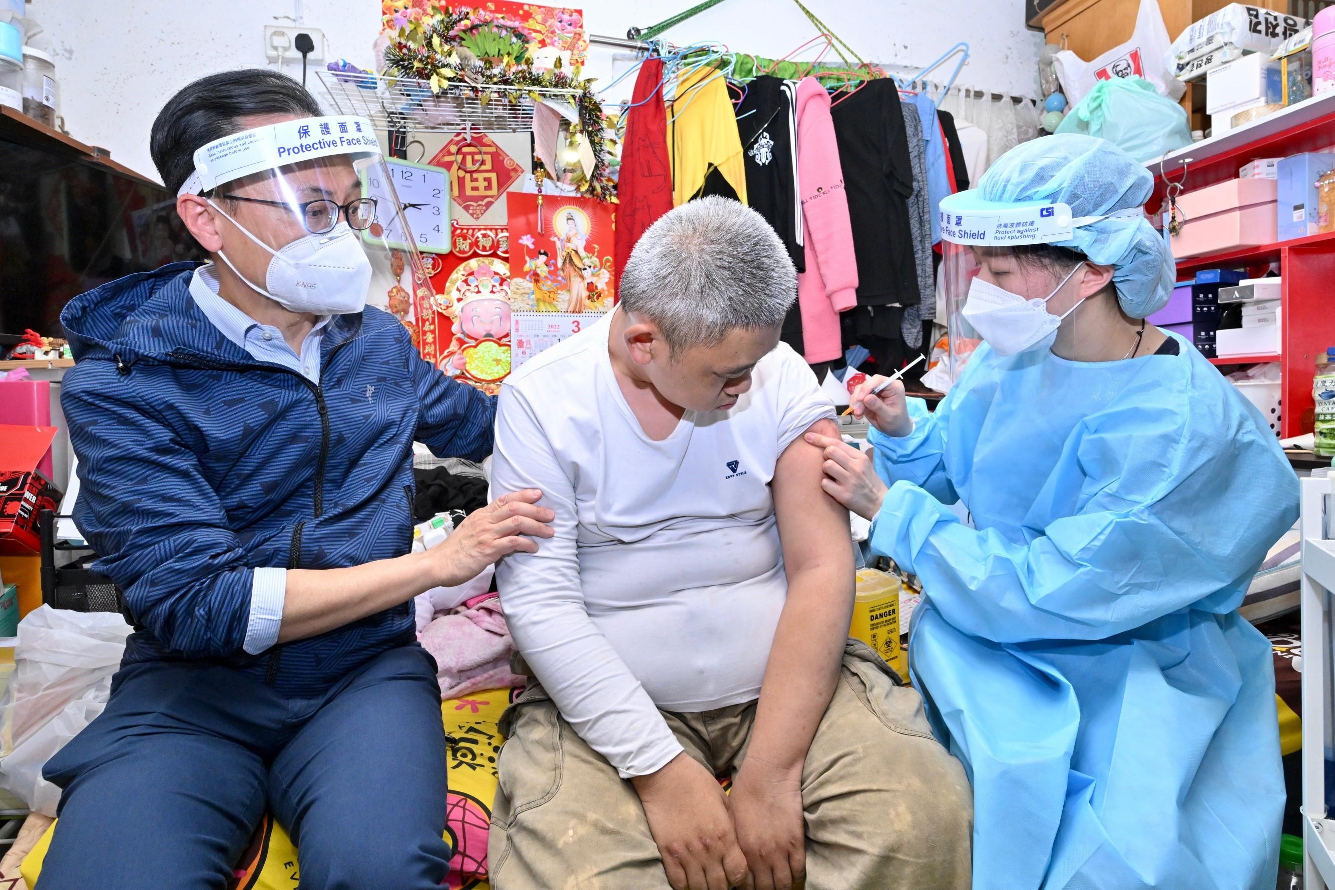 The Government has for the first time arranged a medical team to visit Sun Kit House, Sun Chui Estate in Sha Tin, to conduct a trial to provide door-to-door COVID-19 vaccination service to elderly persons aged 70 or above who have yet to get vaccinated and persons who are unable to leave their homes for vaccination due to illness or physical disability today (March 31). Photo shows a resident with special needs (centre) receiving the COVID-19 vaccine. Looking on is the Secretary for the Civil Service, Mr Patrick Nip (left).
