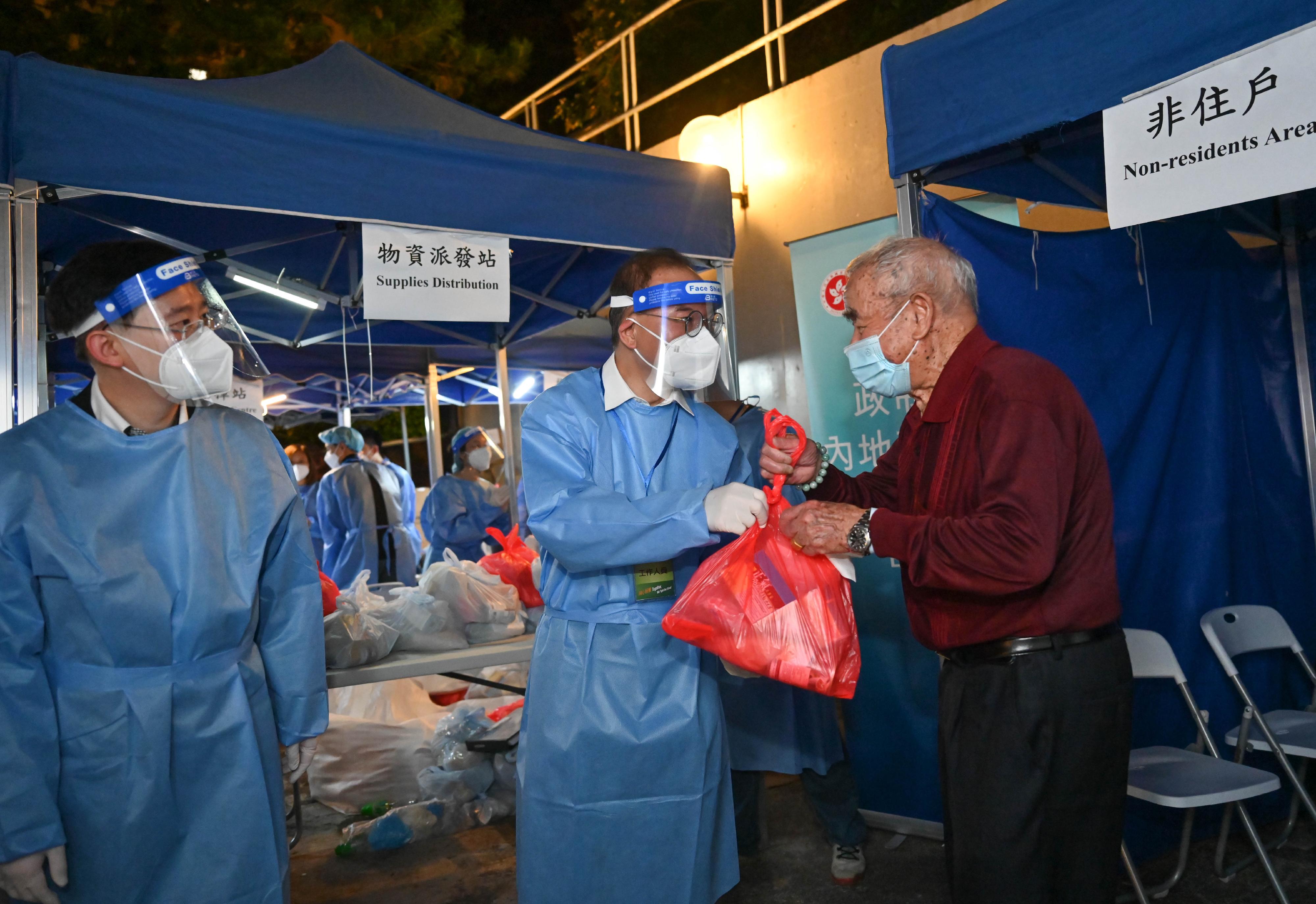 The Secretary for Constitutional and Mainland Affairs, Mr Erick Tsang Kwok-wai, leading an anti-epidemic team formed by about 100 colleagues from the bureau and its department, commenced the "restriction-testing declaration" operation in Block 10, Tsui Chuk Garden, Wong Tai Sin, last night (April 13). Photo shows Mr Tsang (centre), and the Under Secretary for Constitutional and Mainland Affairs, Mr Clement Woo (left), distributing anti-epidemic supplies to a resident subject to compulsory testing.
