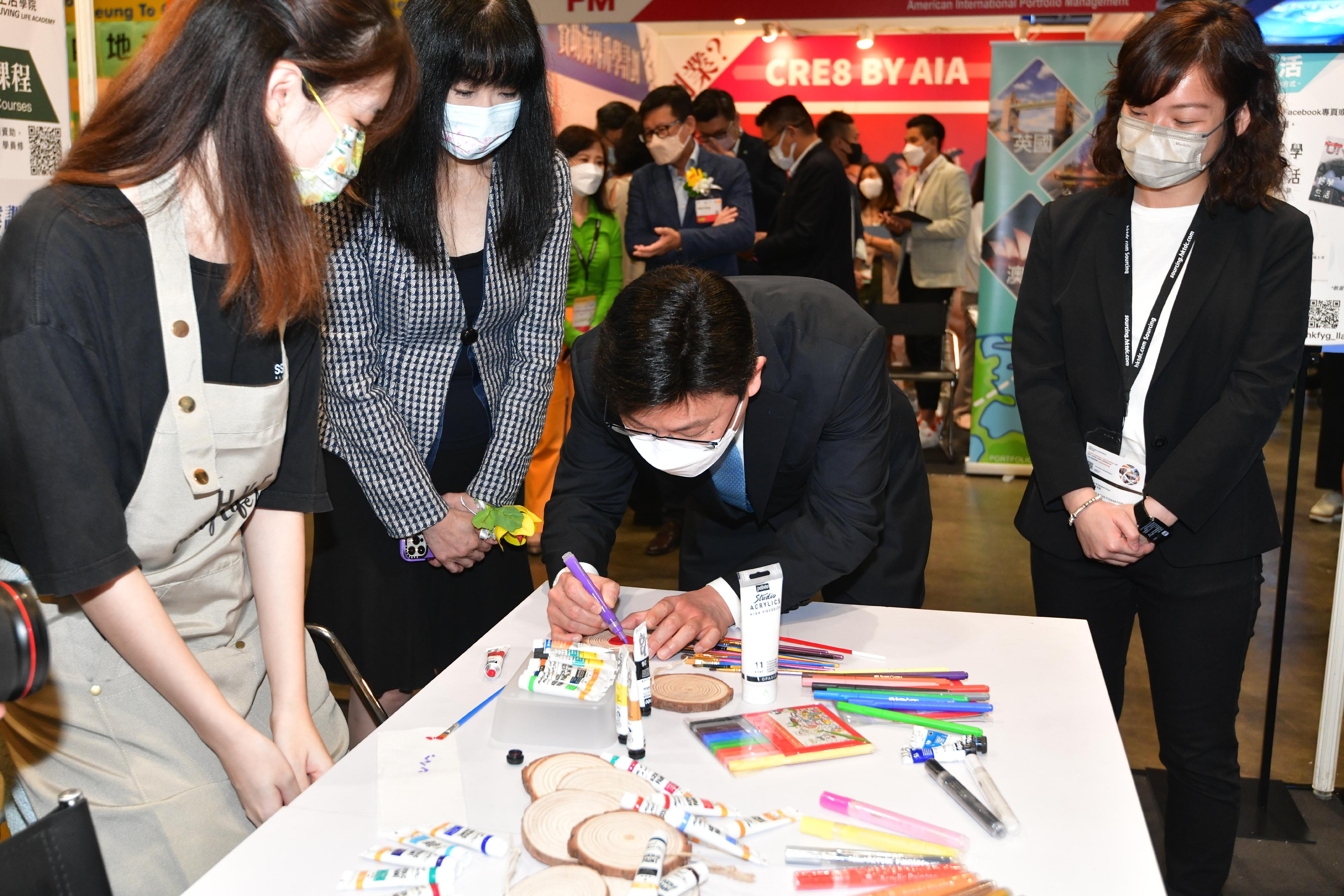 The Secretary for Labour and Welfare, Mr Chris Sun, officiated at the opening ceremony of the Hong Kong Trade Development Council Education & Careers Expo 2022 today (July 21). Photo shows Mr Sun (second right) making souvenirs to encourage youths at the Hong Kong Federation of Youth Groups booth.