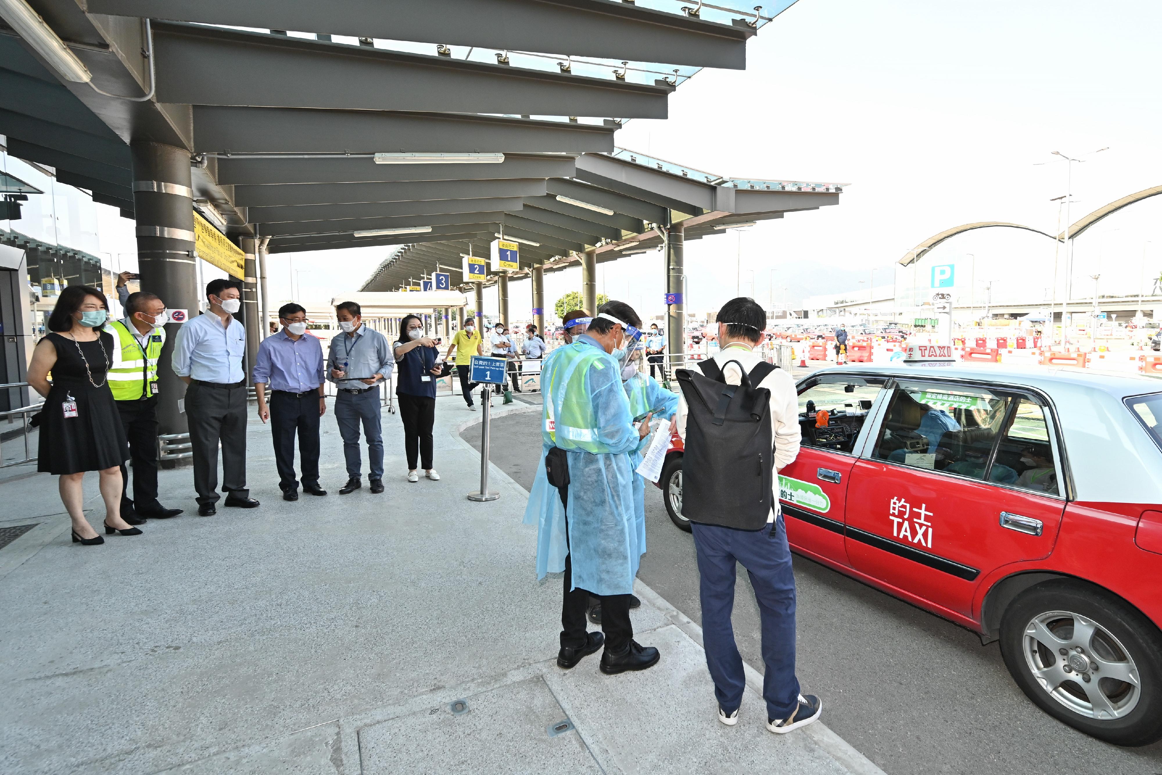 On the first day (July 25) of the trial run of the self-paid designated quarantine hotel (DQH) taxi services, the Secretary for Transport and Logistics, Mr Lam Sai-hung (fourth left), and the Deputy Secretary for Health (Special Duties), Mr Vincent Fung (third left), view the procedures for inbound persons to take self-paid DQH taxis at Hong Kong International Airport.