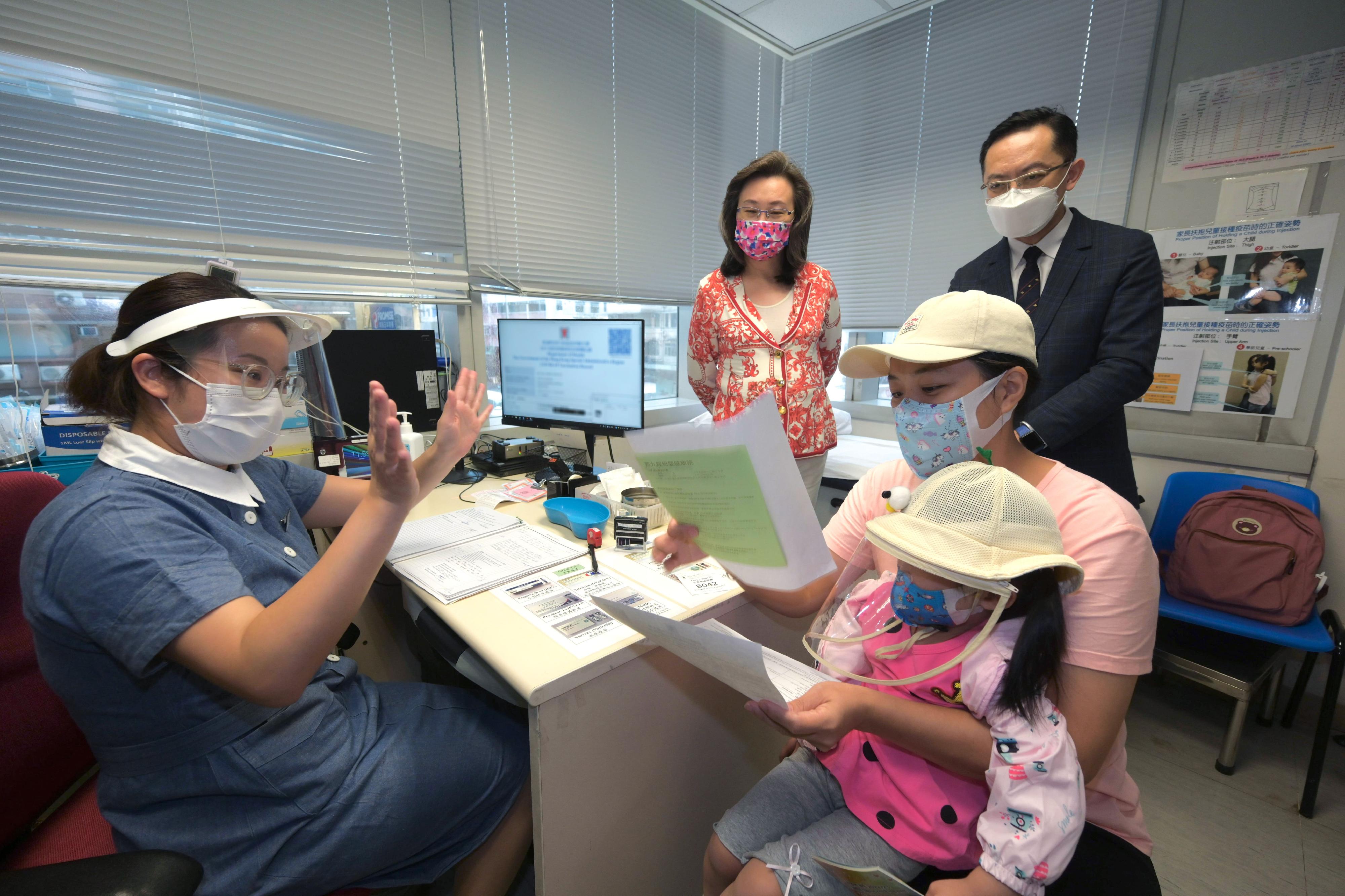 The Secretary for the Civil Service, Mrs Ingrid Yeung, today (August 23) visited West Kowloon Maternal and Child Health Centre to learn about the arrangements of providing a COVID-19 vaccination service for children there. Photo shows a young child who was given her vaccination record after getting vaccinated. Mrs Yeung (back row, left); the Director of Health, Dr Ronald Lam (back row, right); and the nurse who administered the vaccine gave encouragement to the child.