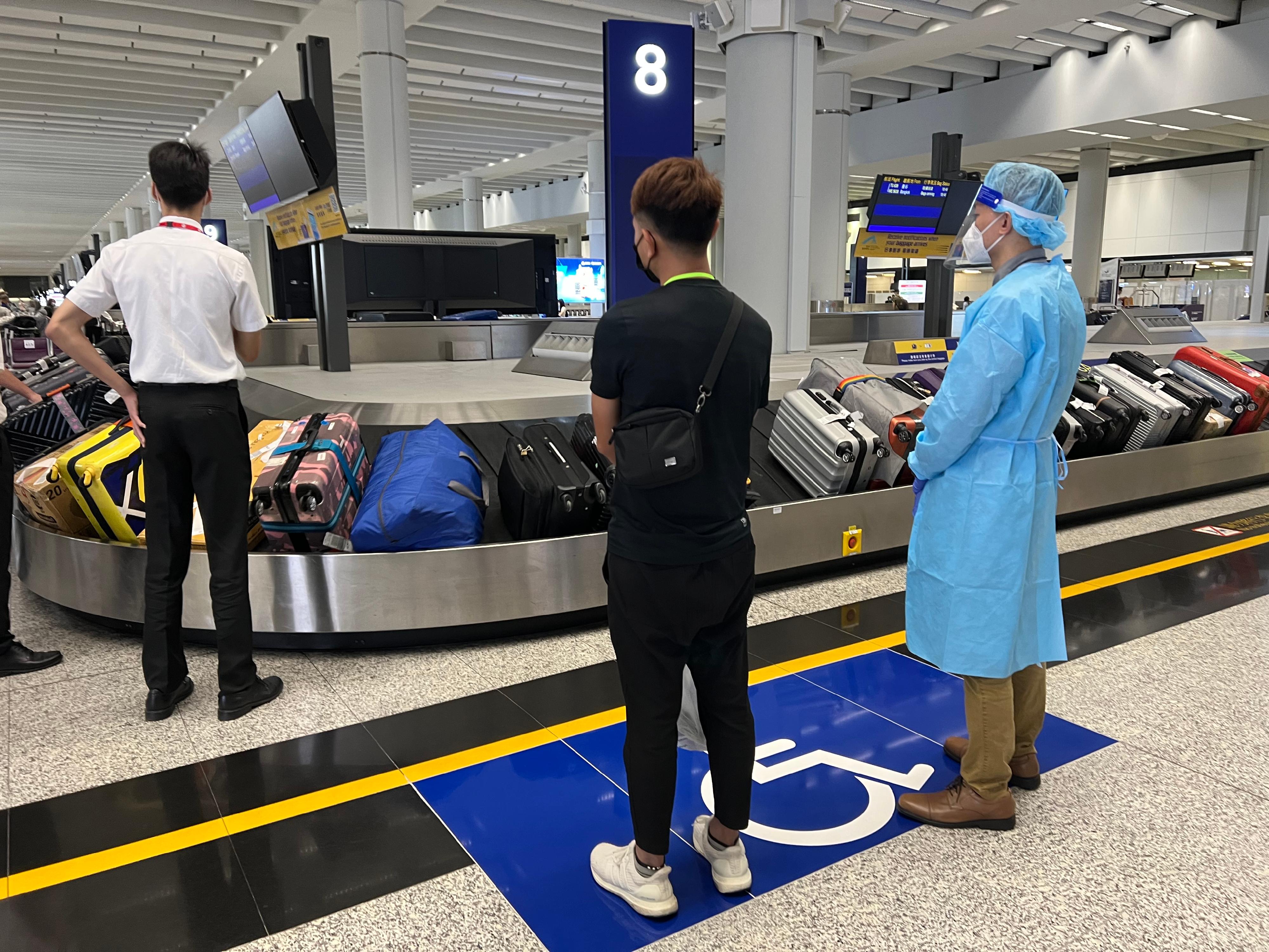 今日（八月二十五日）三名求助港人安全抵达香港国际机场。图示穿上防护装备的入境处人员，协助有关求助港人领取行李。