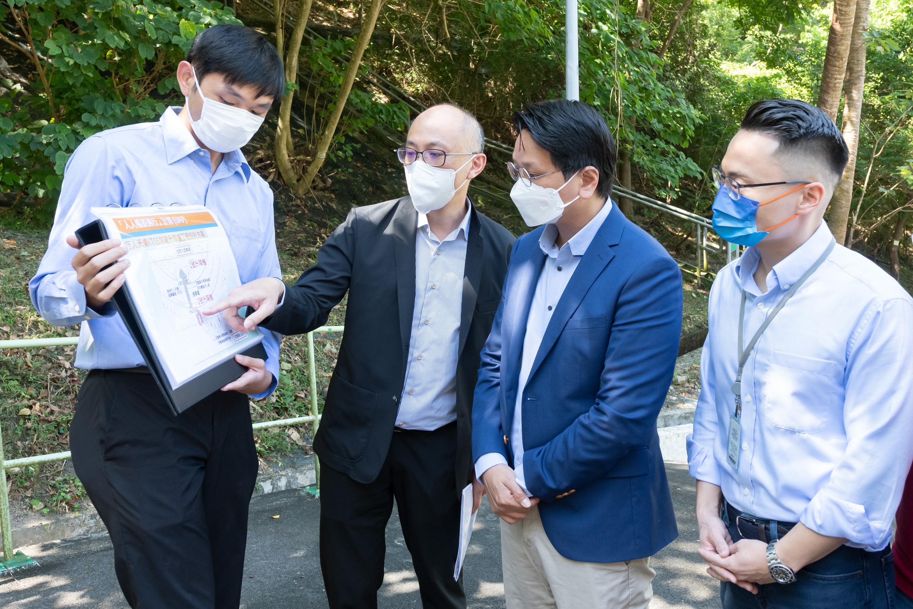 Members of the Legislative Council (LegCo) conducted a site visit at the staircases on the slope of Lok Wah North Estate in Kwun Tong today (October 12) to follow up on a complaint case relating to retrofitting barrier-free access facilities. Photo shows LegCo Members Mr Tang Ka-piu (second right) and Mr Edward Leung (first right) receiving a briefing by government representatives on the progress of the lift installation works at a footbridge near the staircases on the slope of Lok Wah North Estate.