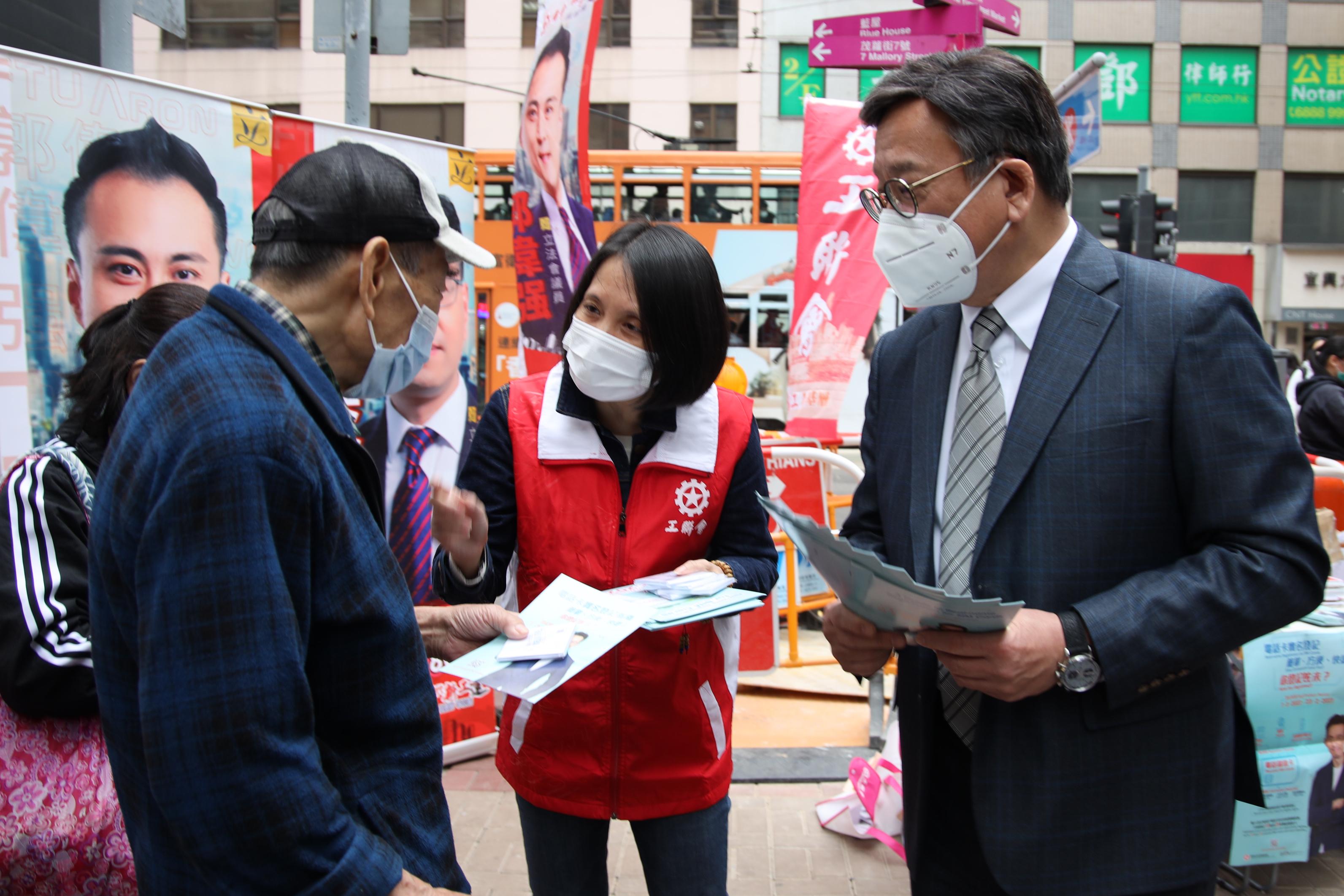 The Secretary for Commerce and Economic Development, Mr Algernon Yau, this afternoon (February 16) visited street counters set up by various district organisations to view their support service for real-name registration for SIM cards. Photo shows Mr Yau (right) distributing promotional items to a member of the public and reminding him to complete the registration before the deadline on February 23.