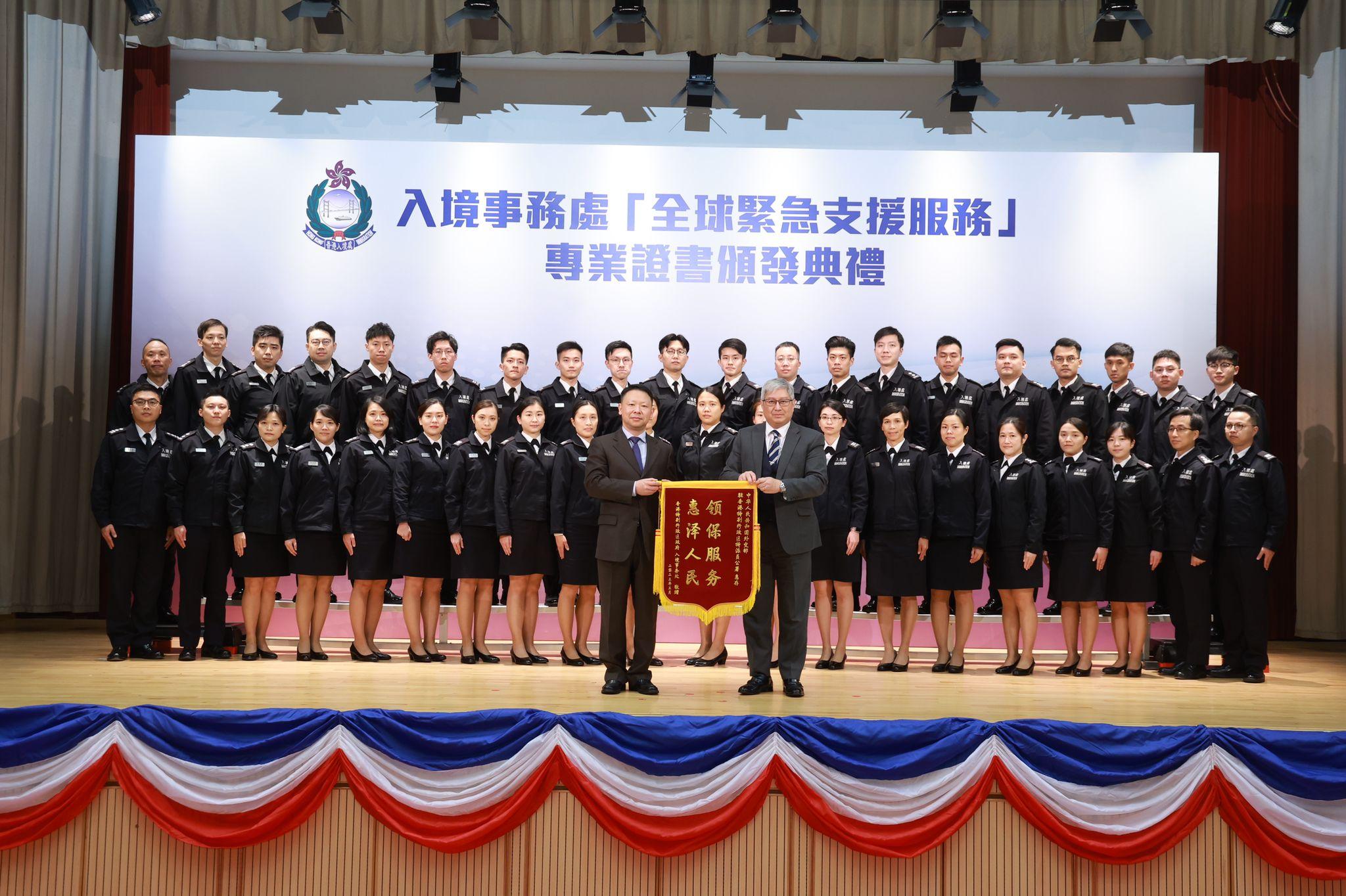The Director of Immigration, Mr Au Ka-wang (front row, right), presents a silk banner to the Deputy Director-General of the Consular Department, Office of the Commissioner of the Ministry of Foreign Affairs in the Hong Kong Special Administrative Region, Mr Zheng Jie (front row, left), at the certificate presentation ceremony for "Professional Certificate in Worldwide Emergency Assistance Services for Immigration Service Members" today (March 28).