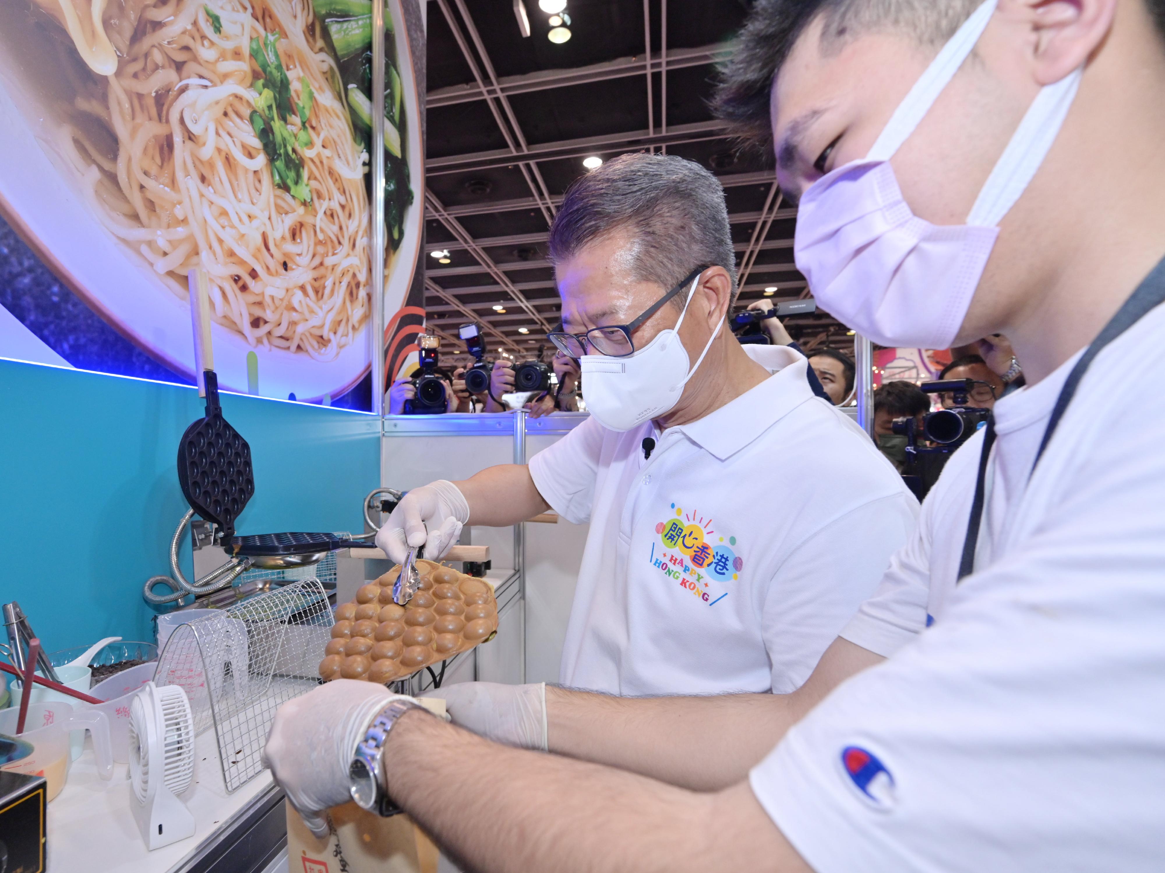 The Financial Secretary, Mr Paul Chan, officiated at the opening ceremony of the first "Happy Hong Kong" Gourmet Marketplace today (April 29). Photo shows Mr Chan (left) preparing egg waffle with an exhibitor.