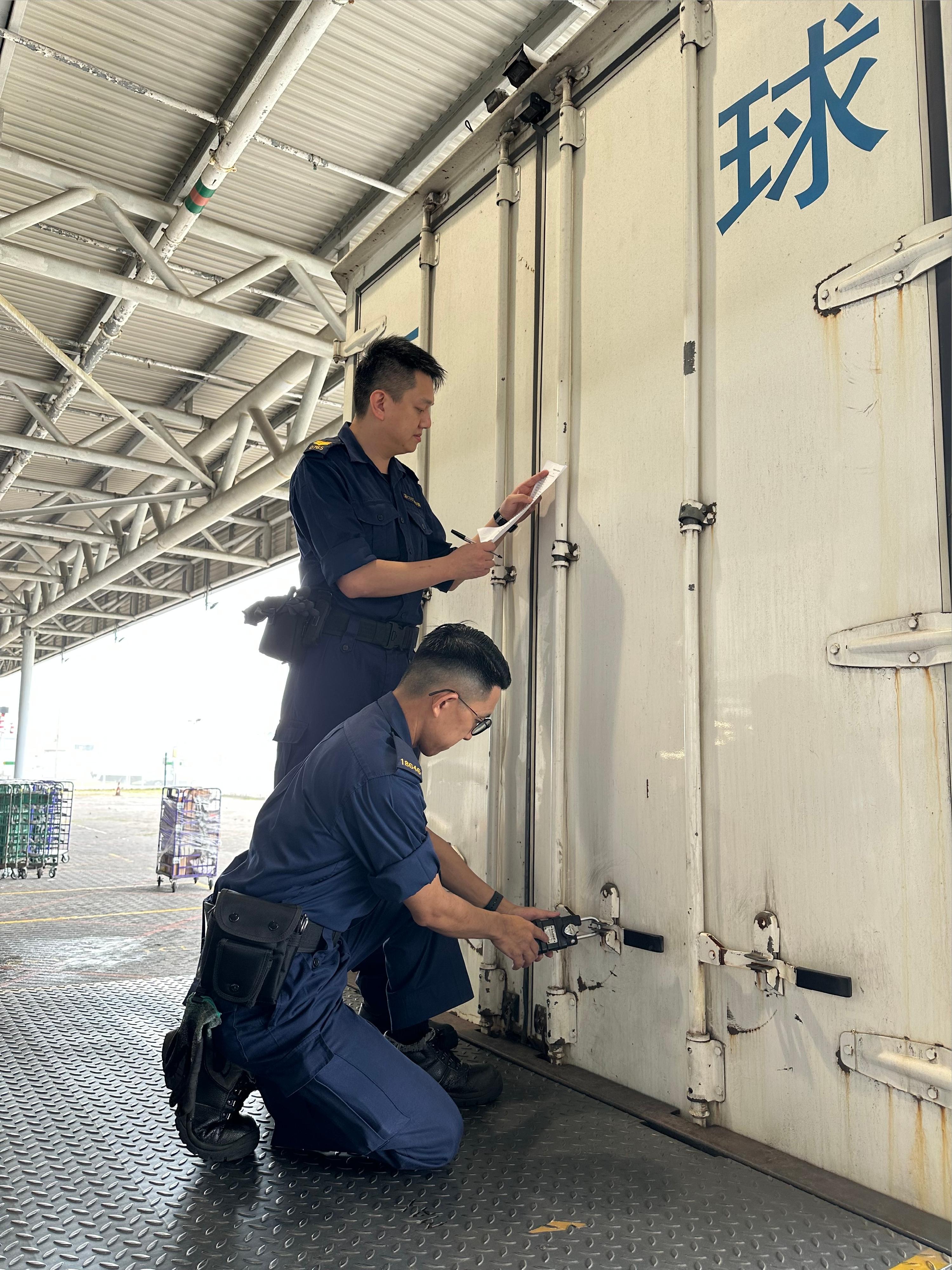 The Hunan-Guangdong-Hong Kong Single E-lock Scheme was officially launched yesterday (June 13) and the first batch of transshipment postal items was successfully delivered to the Hong Kong International Airport Air Mail Centre from Changsha, Hunan today (June 14). Photo shows Hong Kong Customs officers checking the status of the e-lock that is applied to the batch of transshipment postal items. 