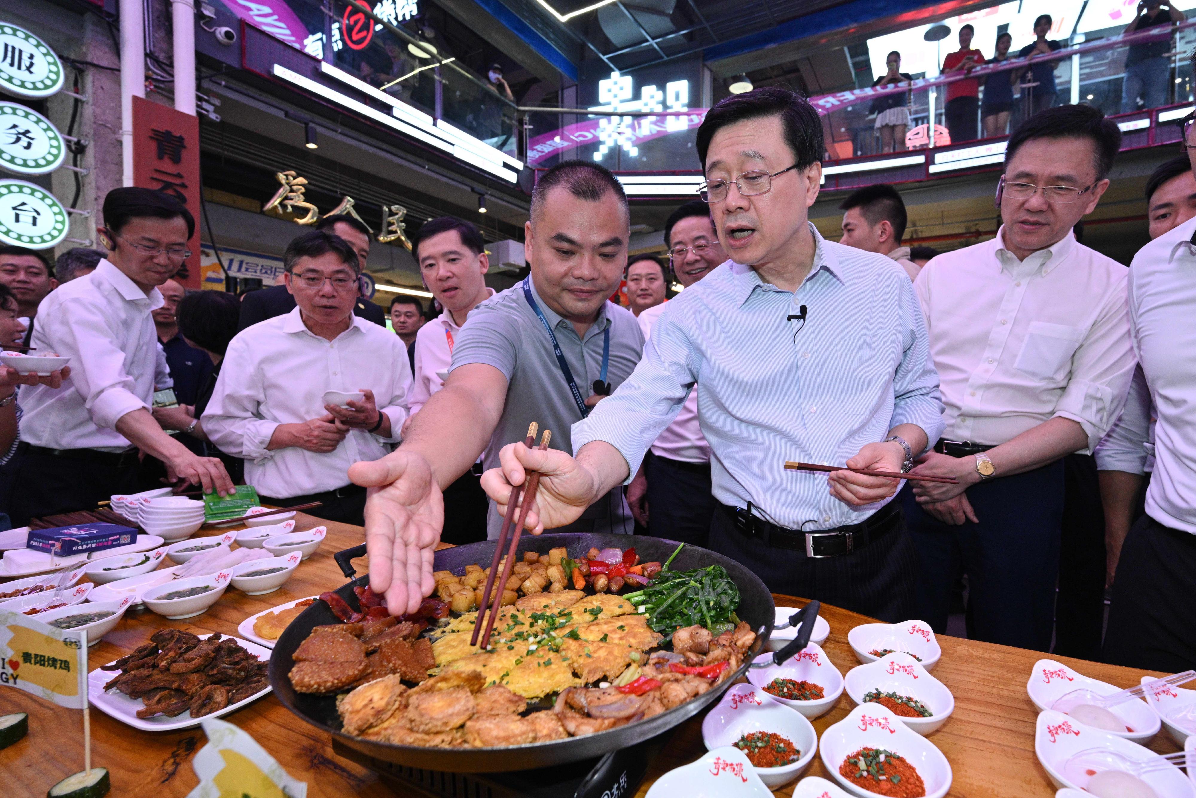 The Chief Executive, Mr John Lee, led a delegation to start his visit programme in Guiyang, today (July 6). Photo shows Mr Lee (second right) tasting local food at the Qingyun Market.