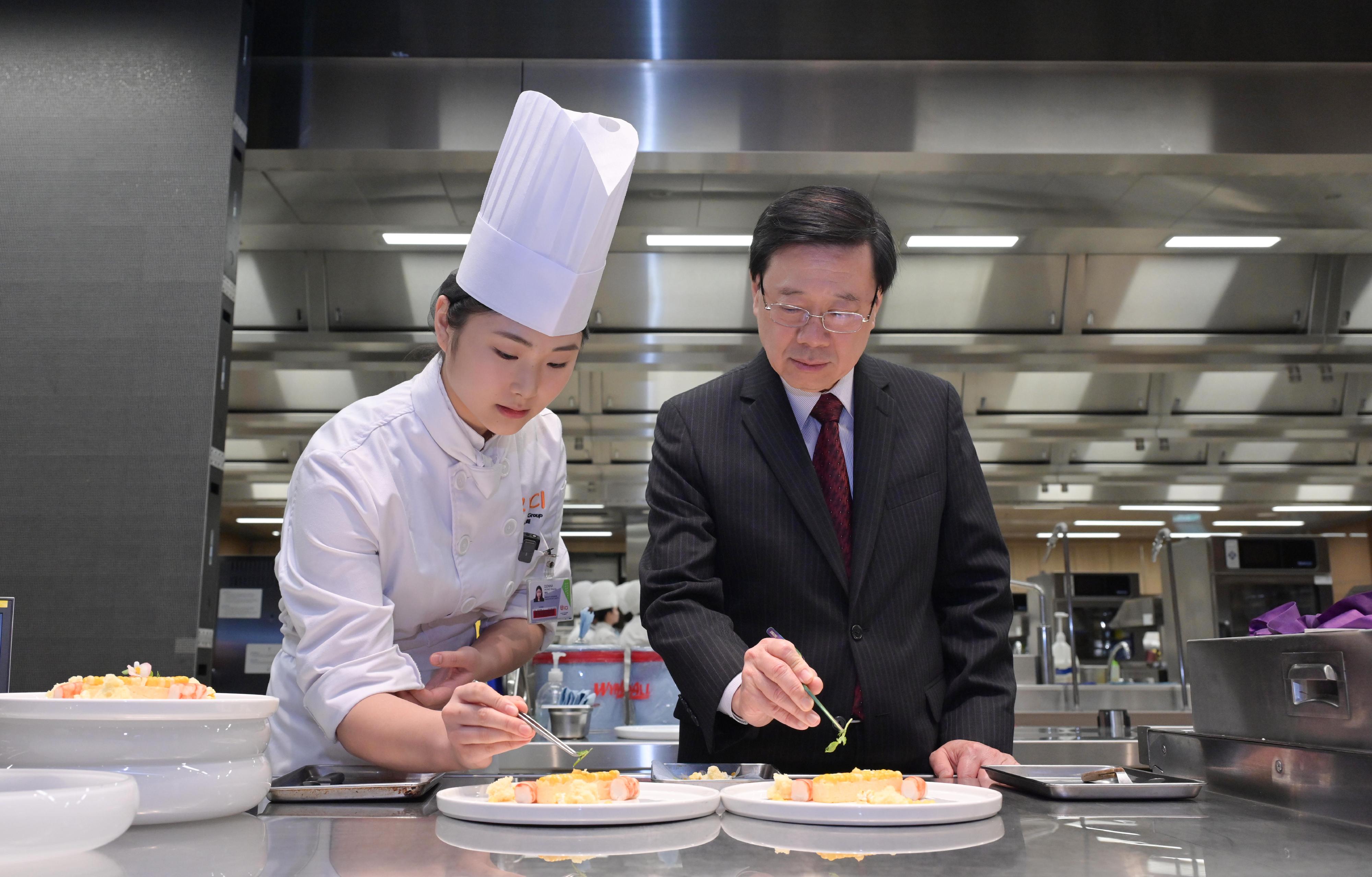 行政長官李家超今日（八月十七日）到訪職業訓練局轄下的國際廚藝學院。圖示李家超（右）在學員的指導下，學習為菜式擺盤。