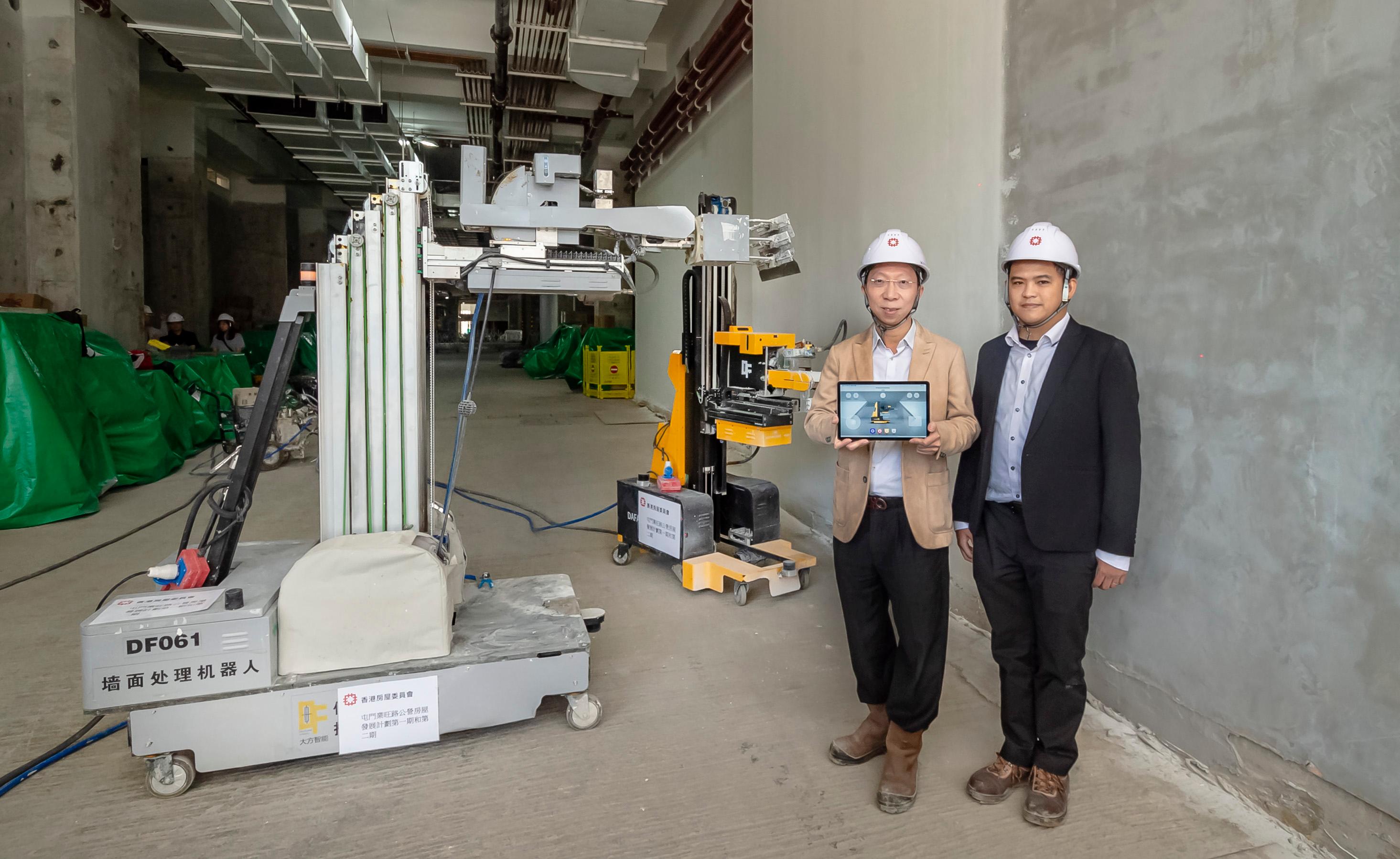 The Hong Kong Housing Authority introduced multifunctional indoor construction robot, the first of its kind, to boost safety at public housing sites. Photo shows the Head/Development and Construction InnoTech, Mr Romeo Yiu (left), and Structural Engineer Mr Arthur Leung (right) of the Housing Department with two multifunctional indoor construction robots.
