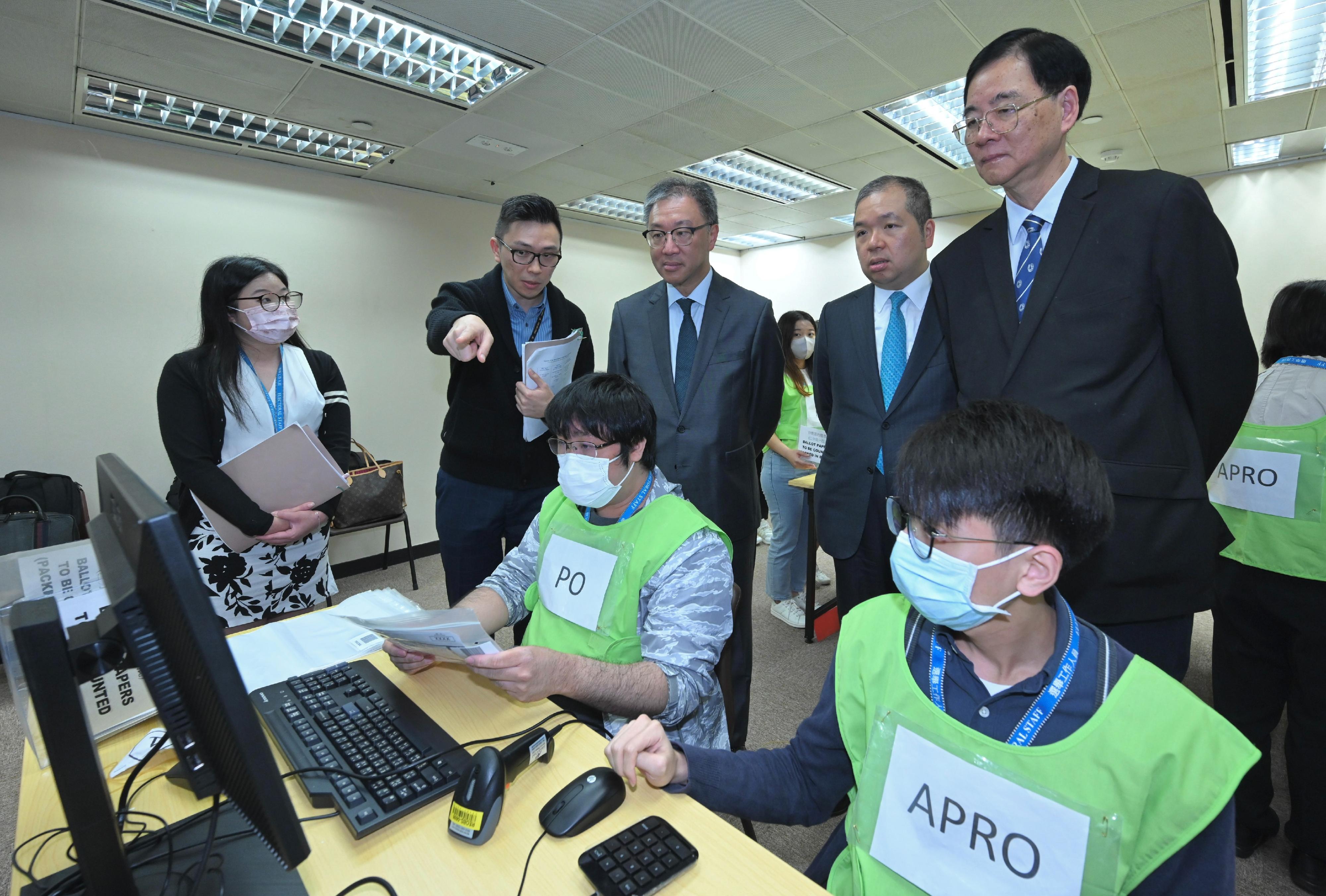 选举管理委员会（选管会）主席陆启康法官今日（十一月二十三日）视察选举事务处的二○二三年区议会一般选举的投票及点票安排示范。图示陆启康法官（后排中）、选管会委员石丹理教授（后排右一）和文本立资深大律师（后排右二）听取选举事务处工作人员讲解地区委员会界别的电脑辅助点票程序。