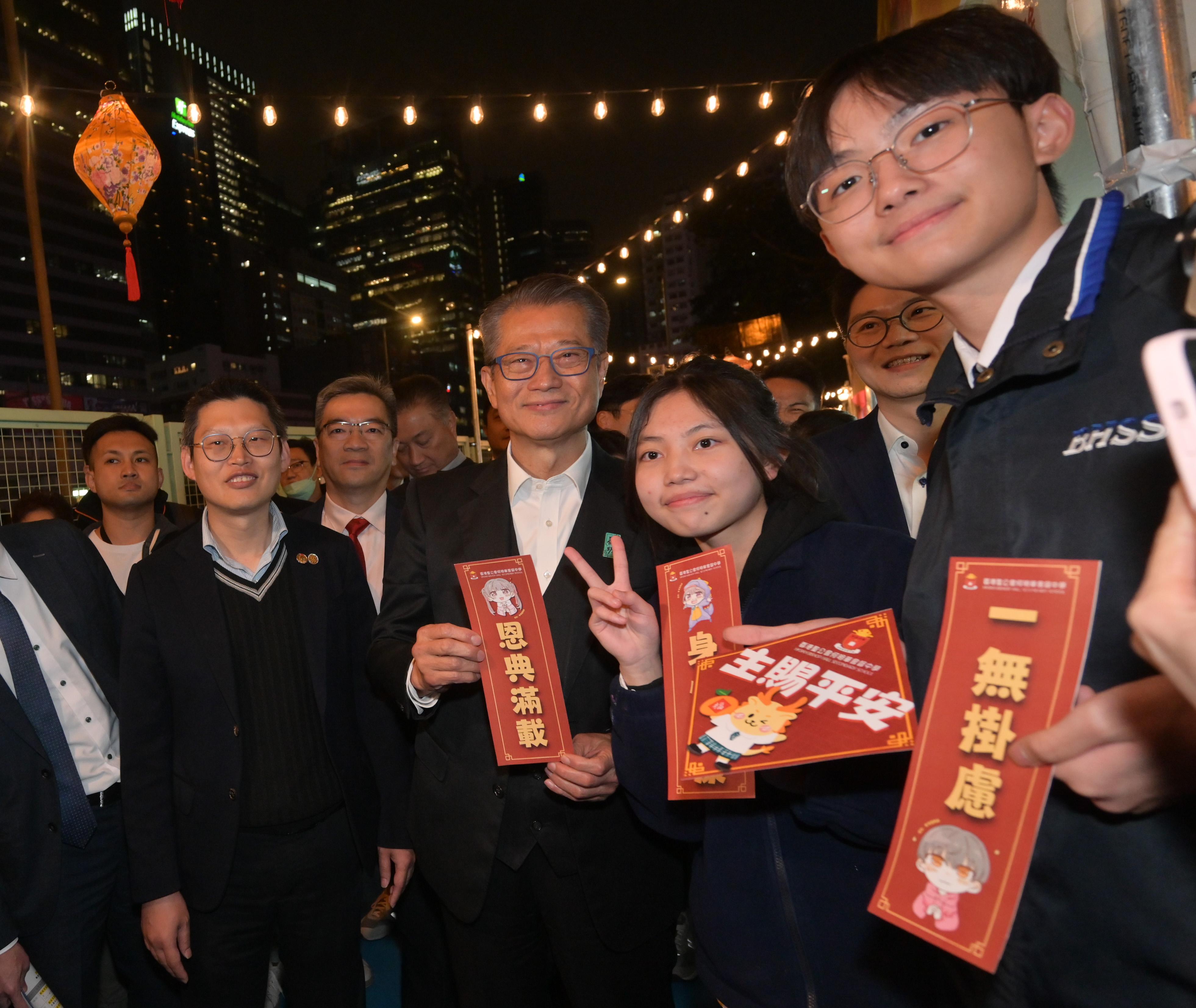 財政司司長陳茂波今日（一月二十九日）出席「龍騰觀塘新春夜市」開幕典禮。圖示陳茂波（右四）在攤檔與學生合照。