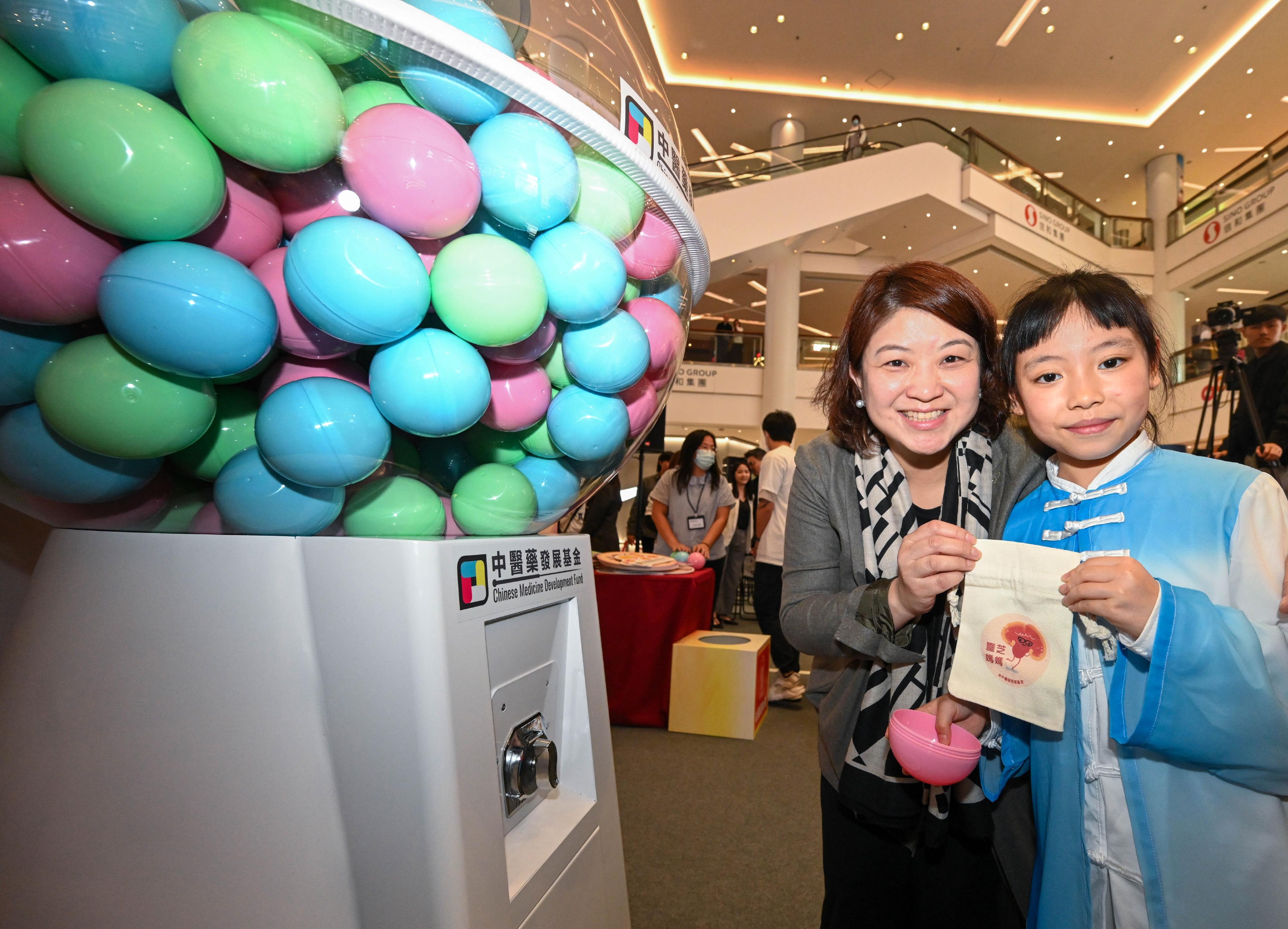 The Chinese Medicine Development Fund commenced a four-day showcase event today (March 8). The Under Secretary for Health, Dr Libby Lee (left), joins a student to redeem souvenir via a gashapon machine.