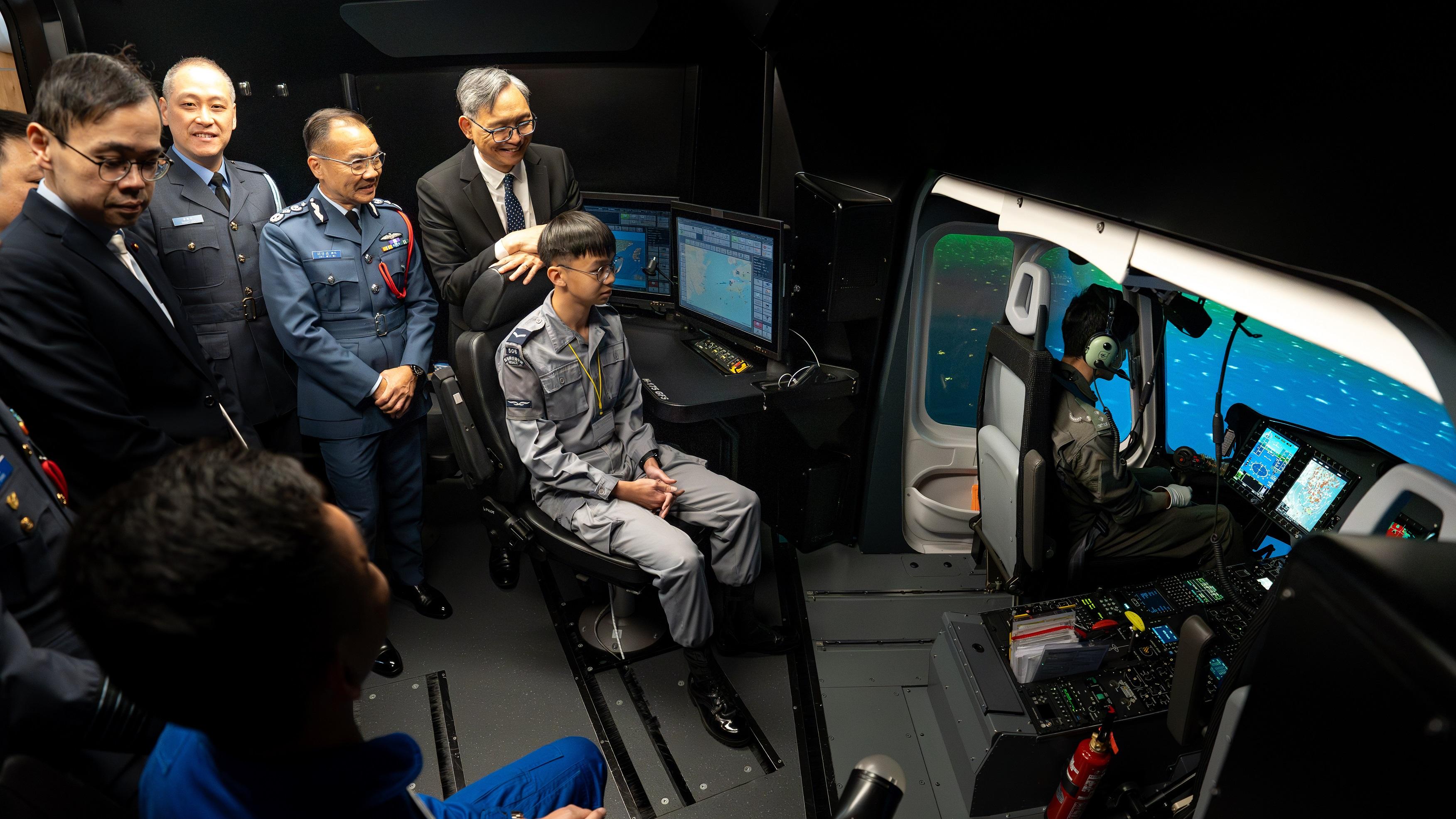 政府飞行服务队与香港航空青年团（航青团）今日（三月九日）签署行政安排备忘录。图示保安局副局长卓孝业（左四）于直升机模拟飞行器与航青团团员交流，了解其学习成果。