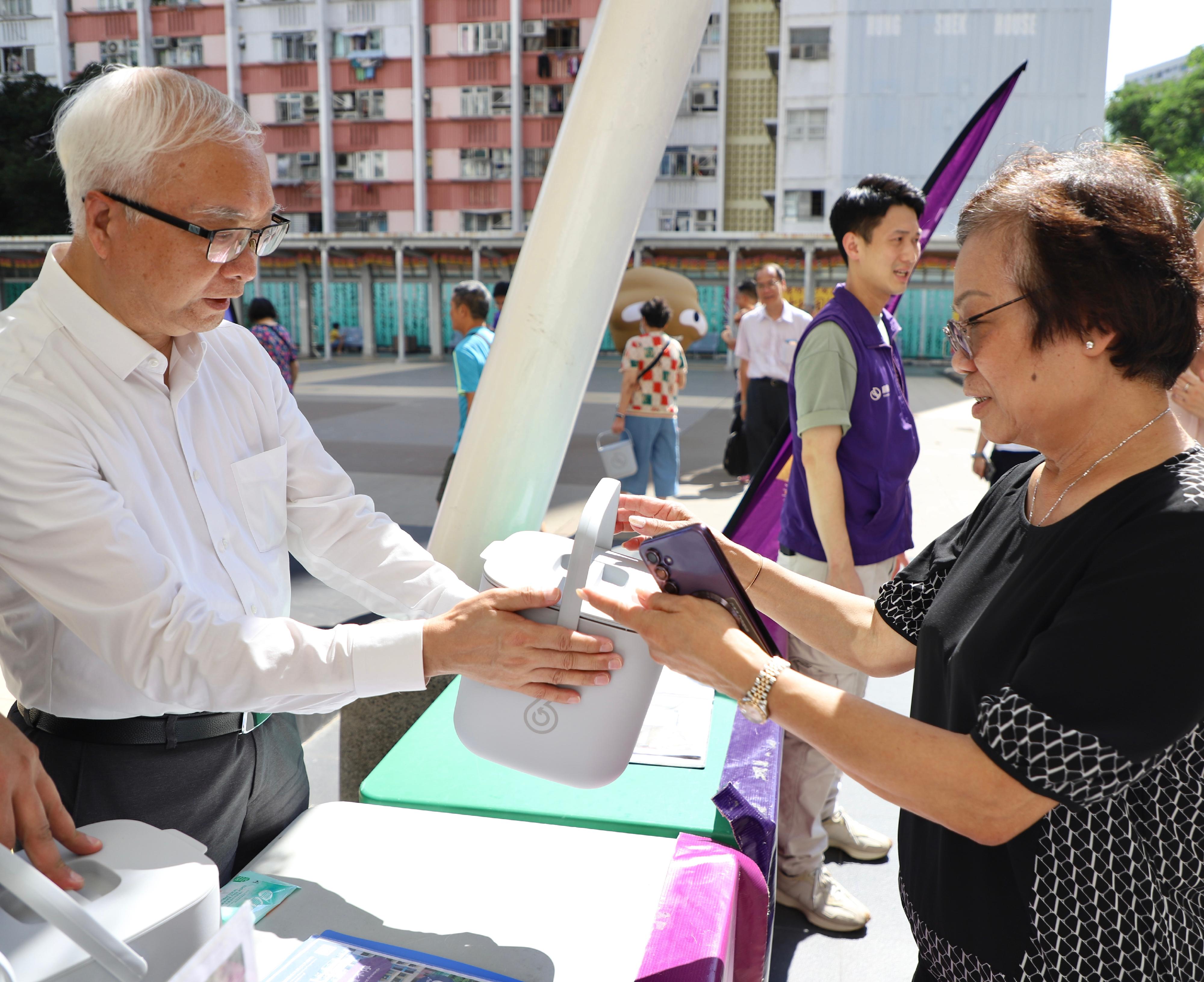 The Secretary for Environment and Ecology, Mr Tse Chin-wan, today (July 4) attended a food waste recycling promotion event held at Ping Shek Estate in Kwun Tong, marking the completion of the expansion of the Environmental Protection Department's food waste collection scheme to all public rental housing estates across the territory, which was accomplished two months ahead of the original target. Photo shows Mr Tse (left) distributing a domestic food waste bucket to a resident.