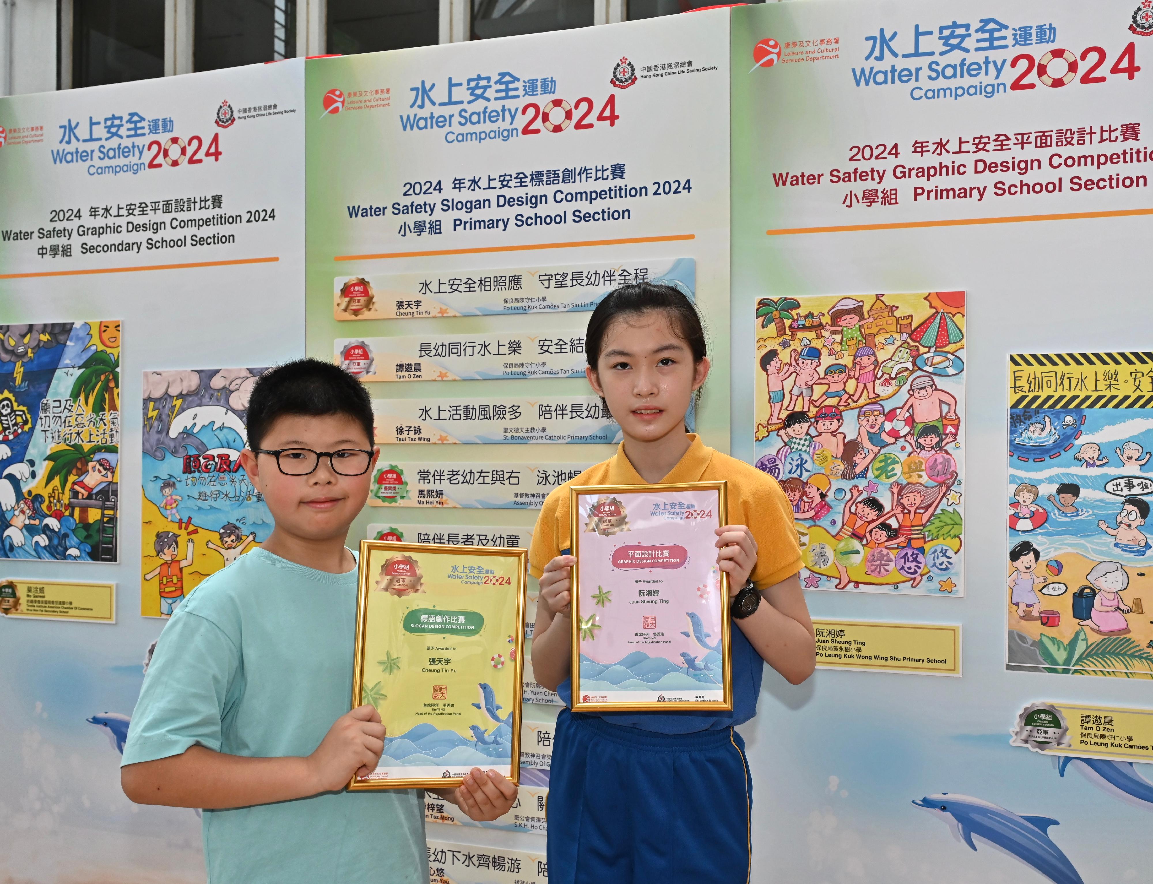 A prize presentation ceremony for the Water Safety Campaign 2024 slogan and graphic design competitions, jointly organised by the Leisure and Cultural Services Department and the Hong Kong China Life Saving Society, was held today (July 6). Pictured with her winning entry is the champion of the primary school section in the graphic design competition, Juan Sheung-ting (right), and the champion of the primary school section in the Chinese slogan competition, Cheung Tin-yu (left).