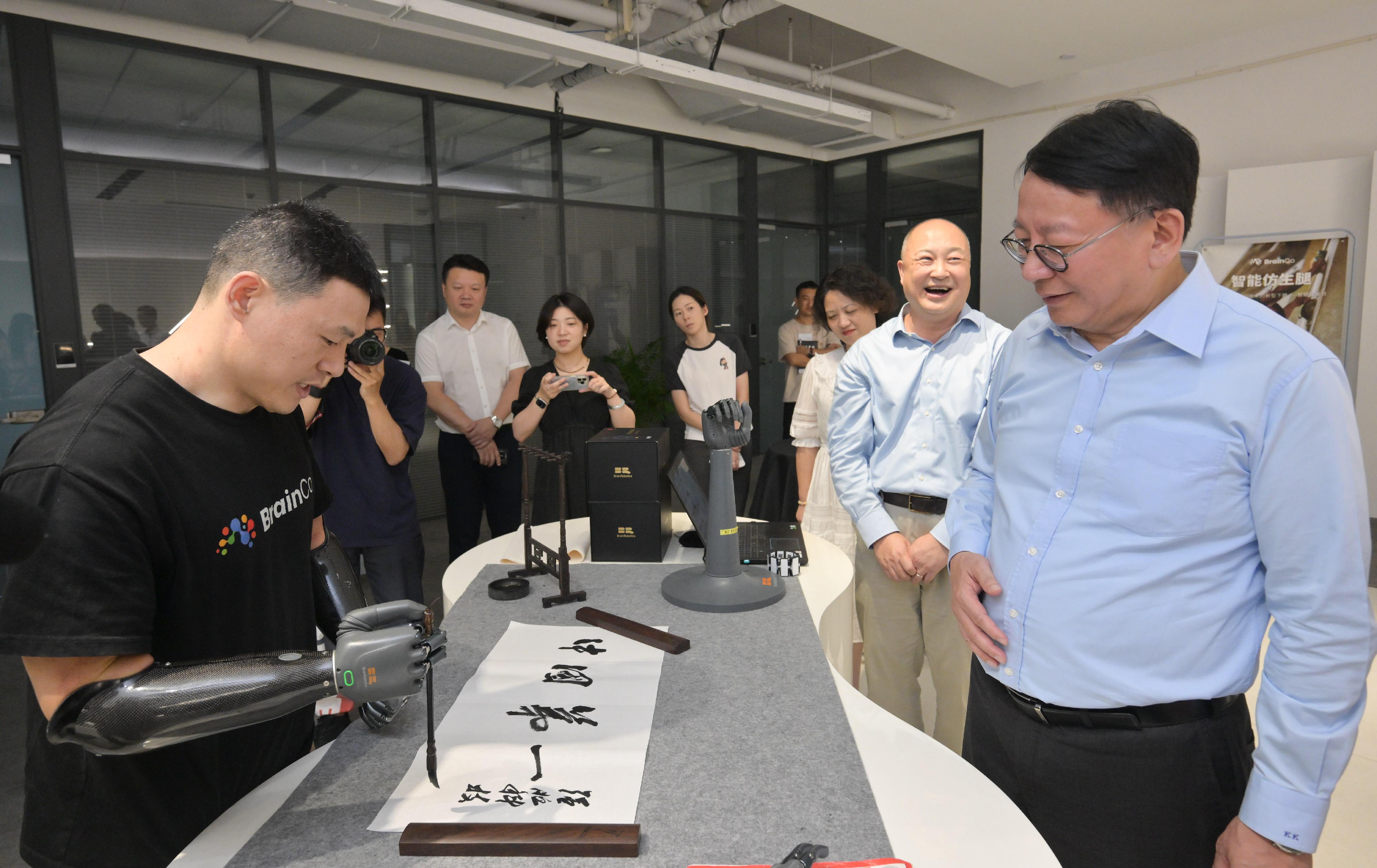 政务司司长陈国基今日（八月十三日）在杭州继续访问行程。图示陈国基（右一）到访高科技初创企业——强脑科技，并观看智能假肢写书法的展示。