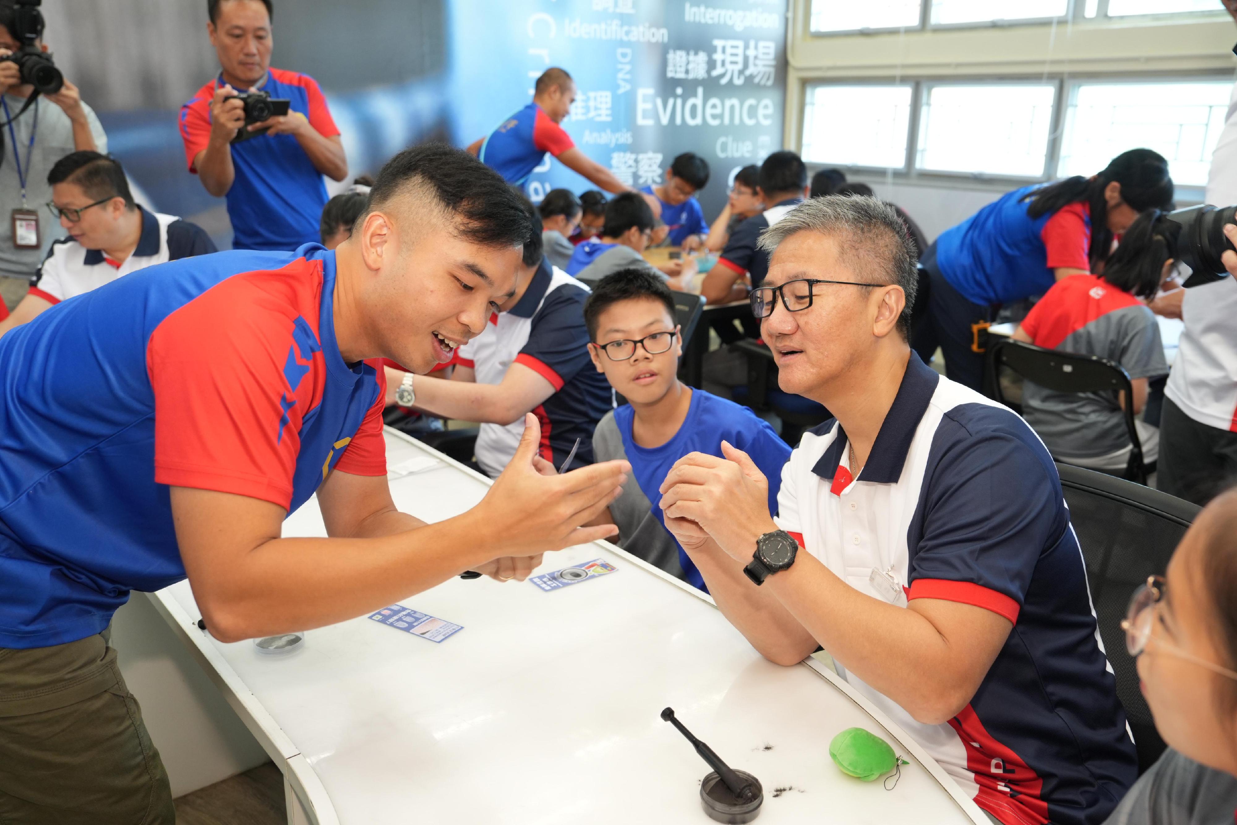 The Opening Ceremony of Junior Police Call Summer Camp 2024 was held today (August 17). Photo shows the Commissioner of Police cum JPC Honorary Deputy Chief President, Mr Siu Chak-yee (first right) taking part in a fingerprint identification workshop with the JPC members.