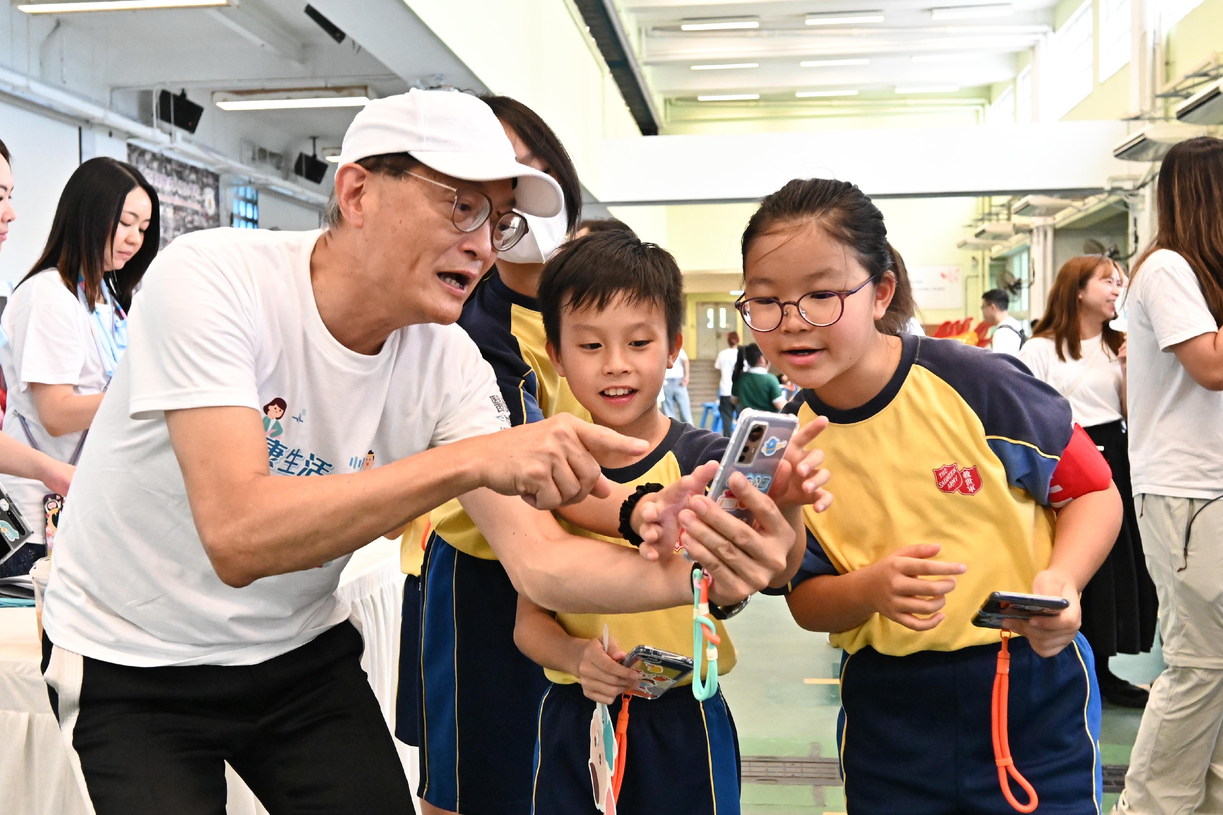 The Secretary for Health, Professor Lo Chung-mau, officiated at the launch ceremony of the first health challenge of eHealth, the "e+ Go to Park" game, today (September 14). Photo shows Professor Lo (first left) enjoying playing the game with students to capture virtual characters to replenish "sports energy".