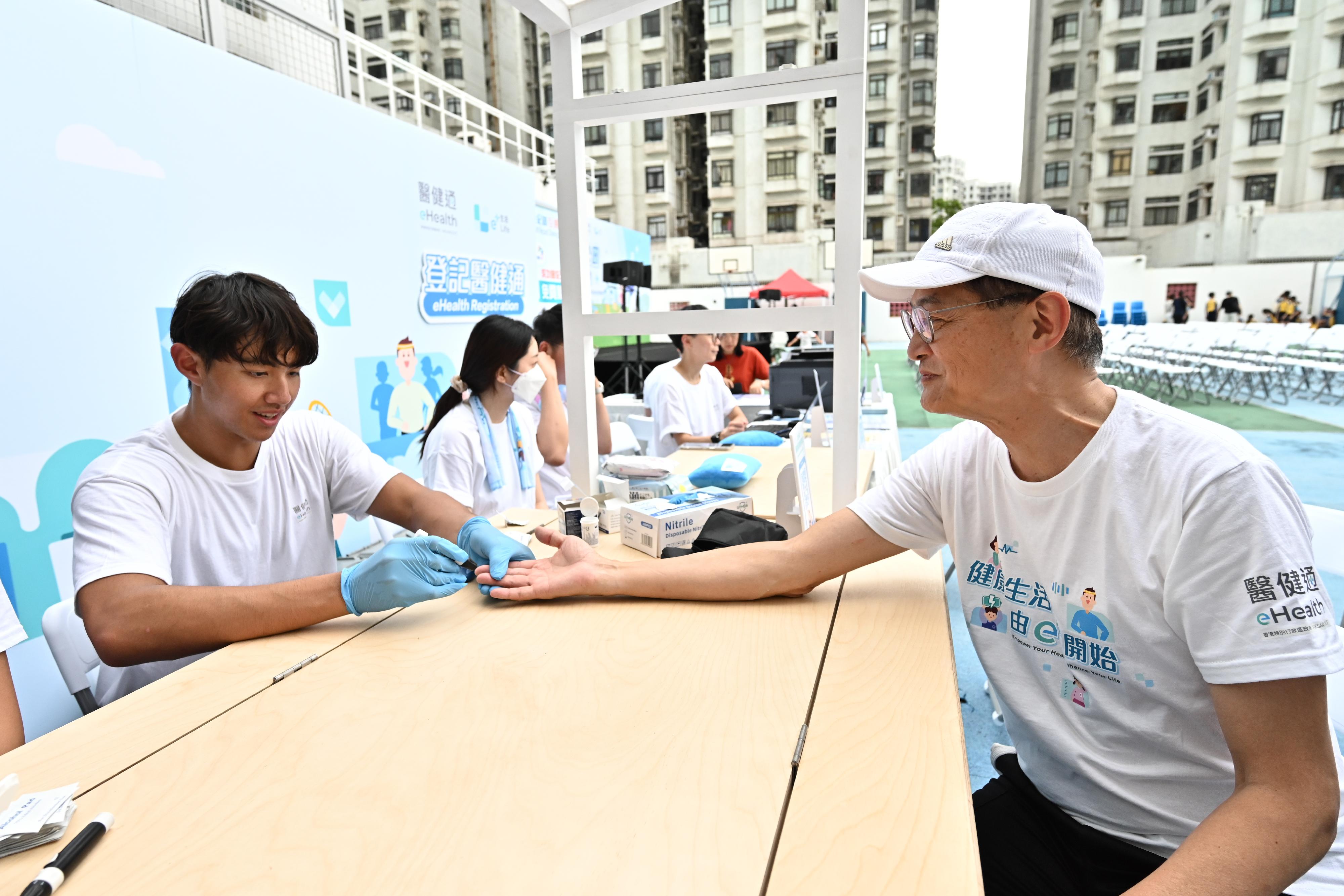 The Health Bureau set up a "e+ Support Station" at the launch ceremony of the first health challenge of eHealth, the "e+ Go to Park" game, today (September 14) to encourage participants to register as eHealth users and have good management of their own health. Photo shows a medical student from the University of Hong Kong measuring blood sugar level for the Secretary for Health, Professor Lo Chung-mau (right).