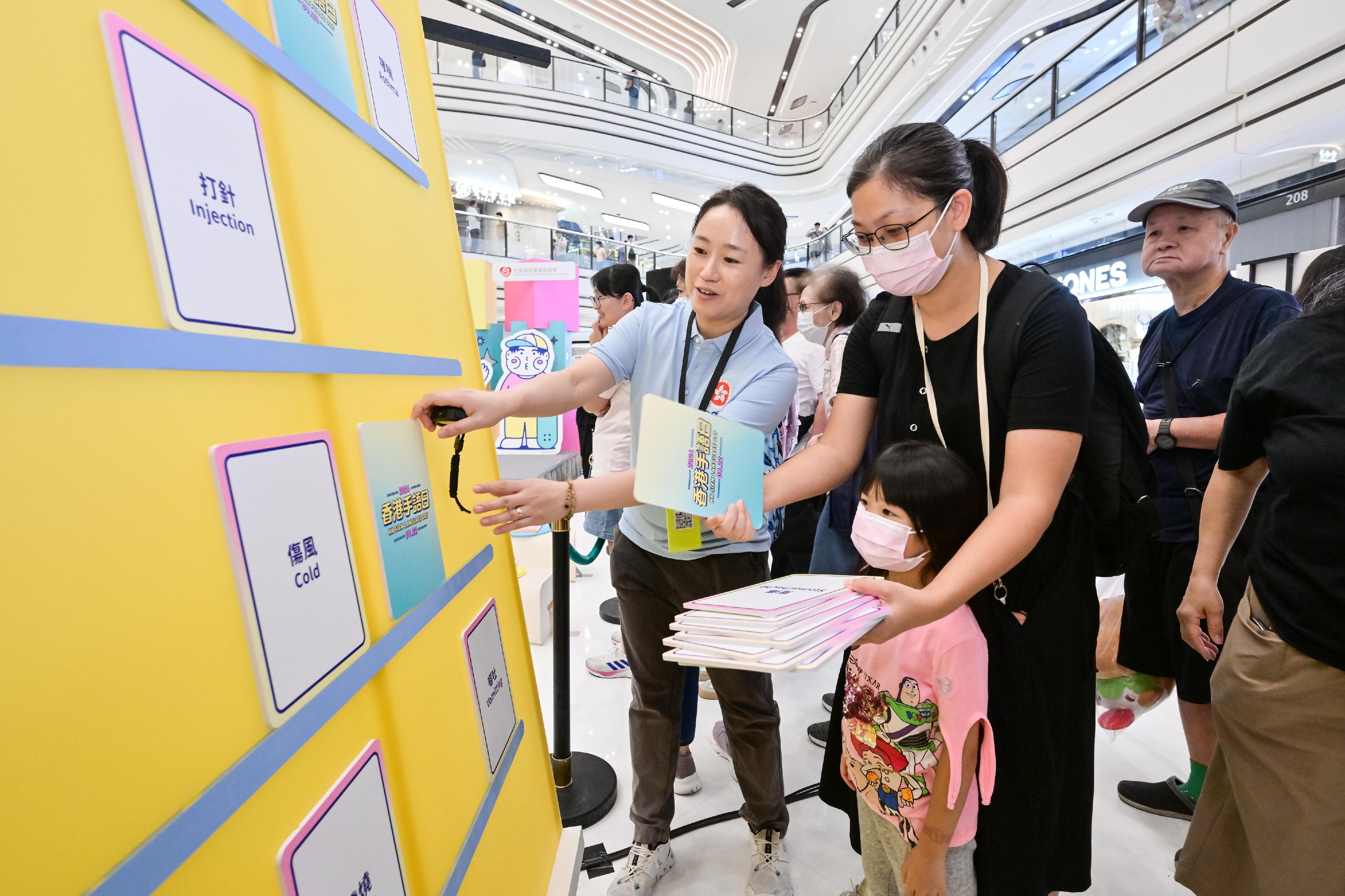 公务员事务局义工队今日（九月二十二日）协助香港聋人福利促进会「香港手语日2024」在大围商场举办摊位活动，让更多市民参与手语学堂、体验活动和游戏之余，亦鼓励他们多与听障人士沟通。图示一名公务员事务局义工队队员协助市民参与摊位游戏。


