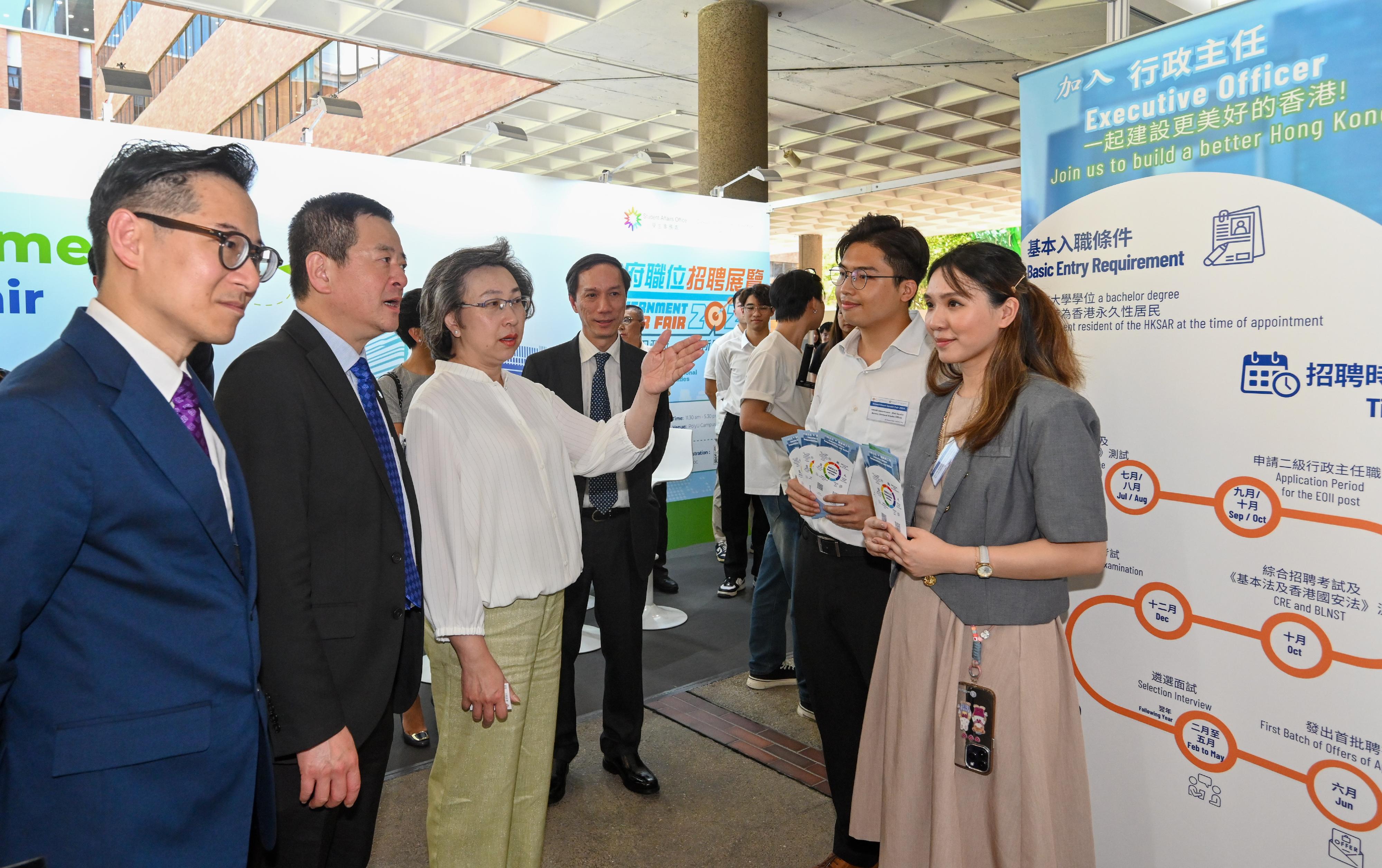 公务员事务局局长杨何蓓茵今日（九月二十六日）到香港理工大学（理大）出席政府职位招聘展览。图示杨何蓓茵（左三）在行政主任职系资讯摊位与两位毕业于理大的行政主任交谈。他们担任是次展览的行政主任招聘大使，鼓励同学申请相关职系。旁为理大副校长（学生及环球事务）杨立伟教授（左二）。