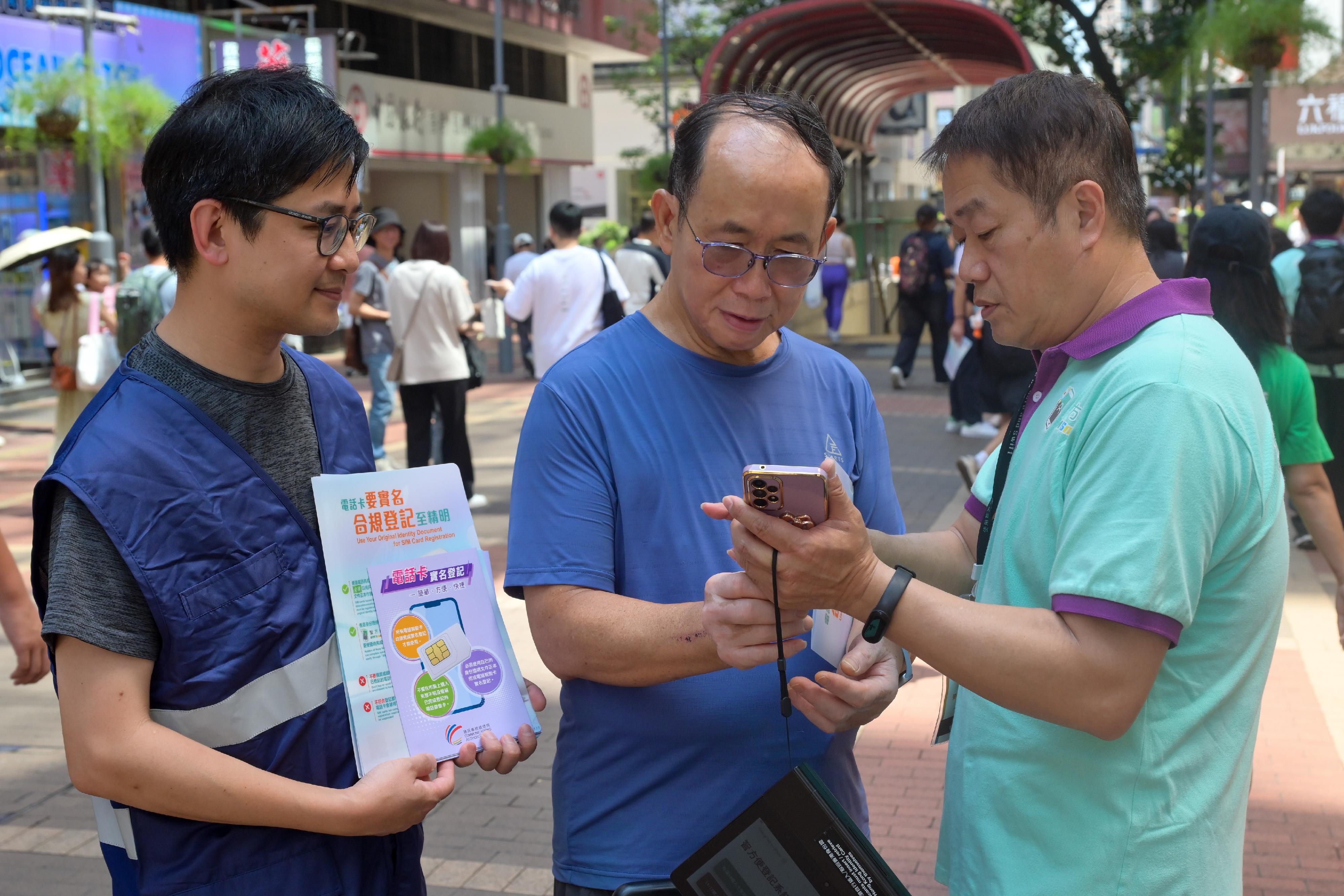 The Office of the Communications Authority and the Digital Policy Office today (September 27) jointly conducted publicity and education activities on the Real-name Registration Programme for SIM Cards in Mong Kok to promote the enhanced arrangement of adopting "iAM Smart" as the default registration method for Hong Kong identity card holders in completing real-name registration on telecommunications service providers' online registration platforms. Photos shows a member of the "iAM Smart" mobile registration team (right) providing on-the-spot assistance to a member of the public registering for iAM Smart". 