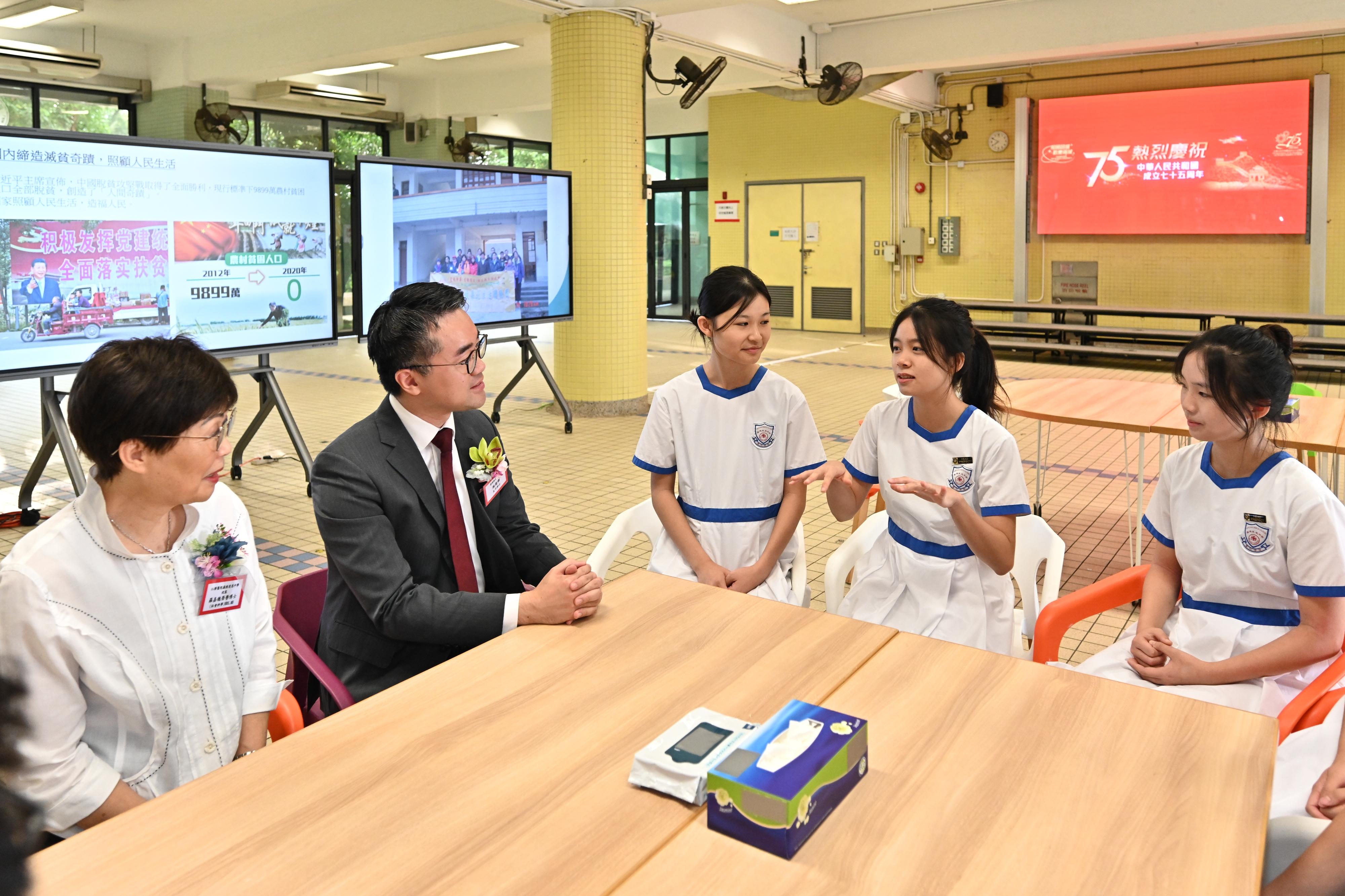 To celebrate the 75th anniversary of the founding of the People's Republic of China, the Education Bureau encourages all primary, secondary schools and kindergartens in Hong Kong to hold before class today (September 30) a national flag-raising ceremony and singing of the national anthem in accordance with the schools' actual situation. The activities are aimed at enhancing students' sense of nationhood, and promoting the spirit of patriotism and national pride among them. Photo shows the Acting Secretary for Education, Mr Sze Chun-fai (second left), chatting with students in Yan Chai Hospital Law Chan Chor Si College.