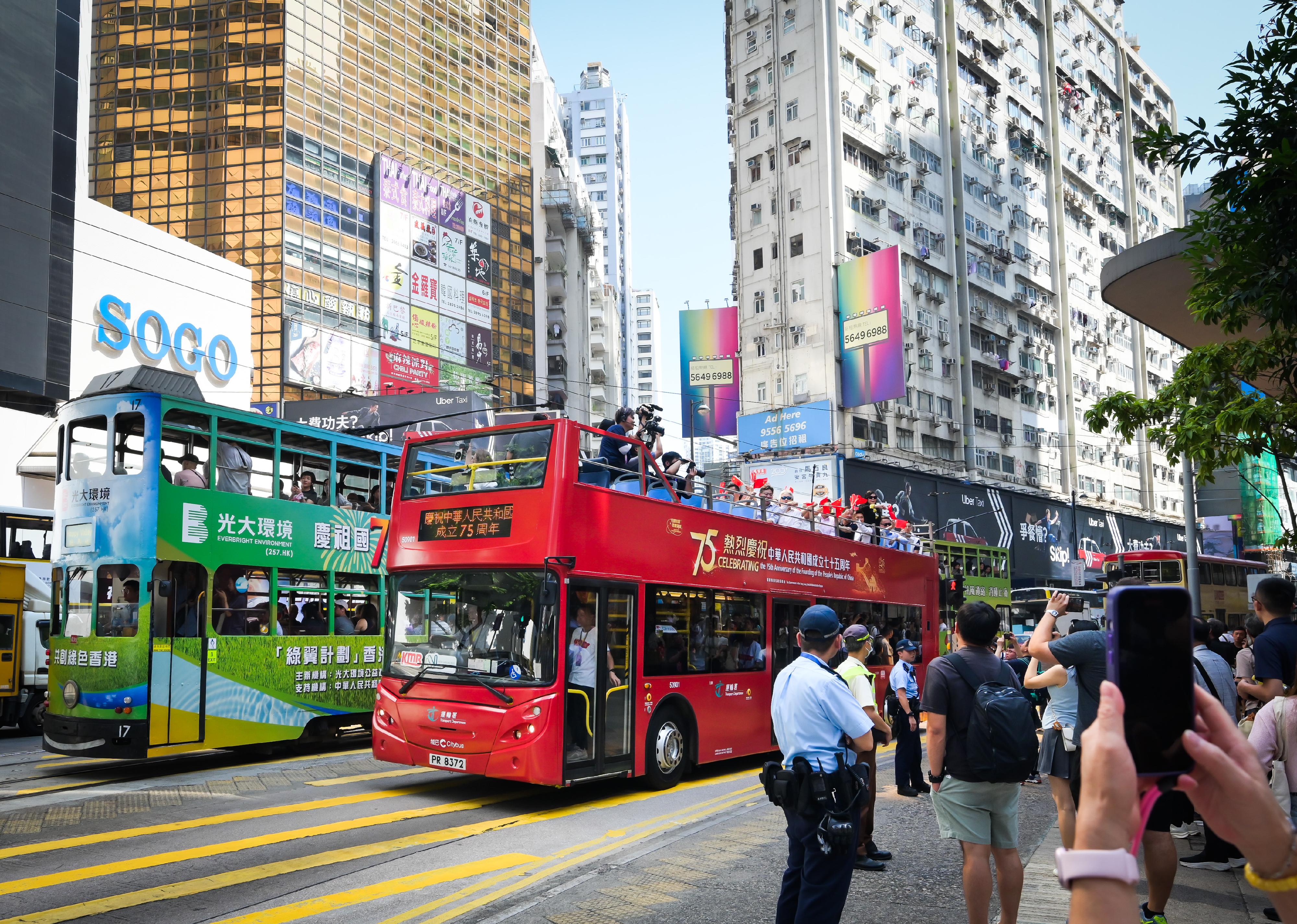 Organised by the Transport Department, the convoy of the Bus Parade for Celebrating the 75th Anniversary of the Founding of the People's Republic of China departed from Victoria Park in Causeway Bay today (October 19). It is one of the highlight events held by the Hong Kong Special Administrative Region Government amid National Day celebrations this year. Photo shows guests engaging with the public and tourists in Causeway Bay on the open-top bus themed on the 75th National Day.