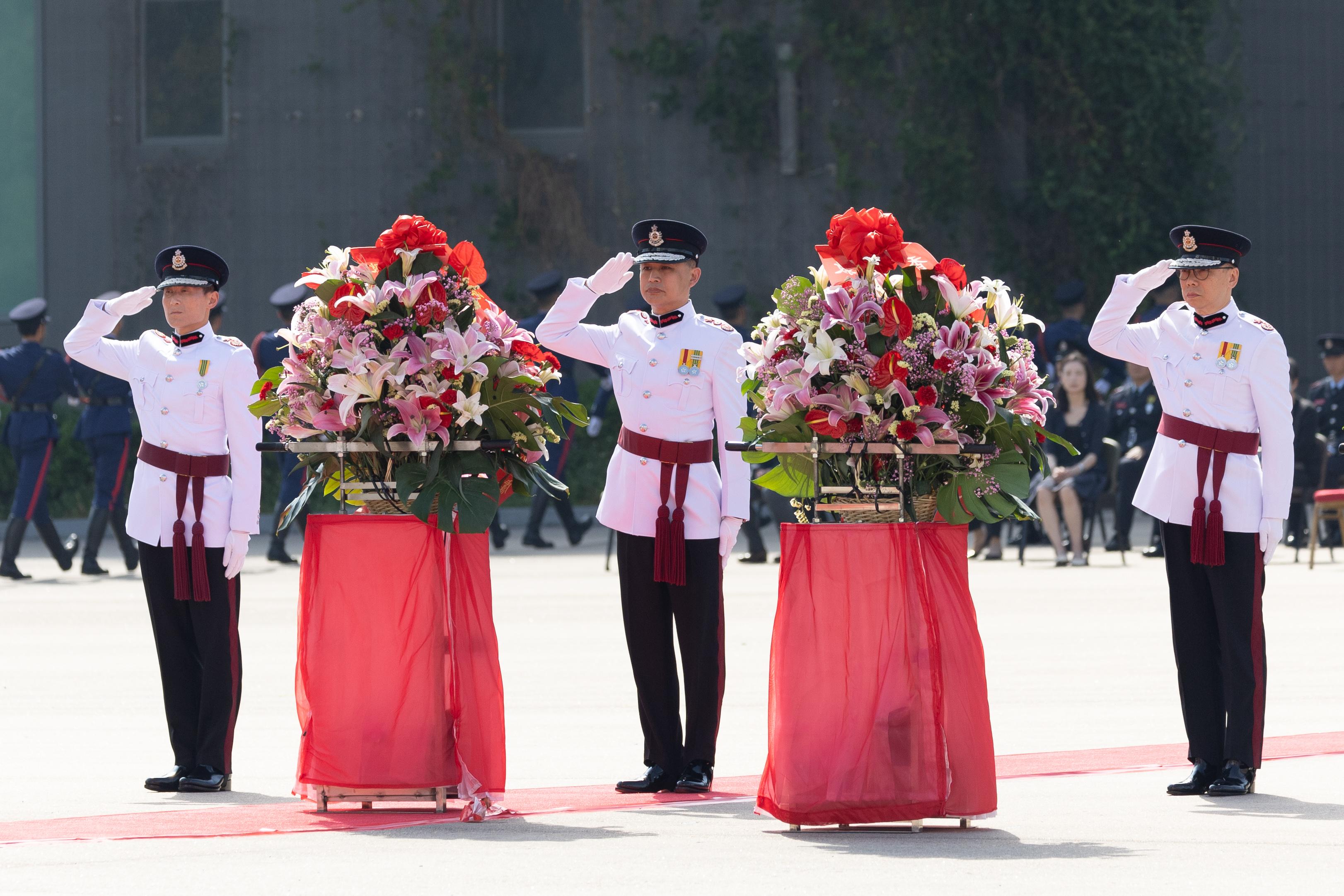 消防處處長楊恩健（中）、副處長（行動）黃鎮業（右）及副處長（公眾安全及機構策略）陳慶勇（左）在儀式上於花籃前敬禮。