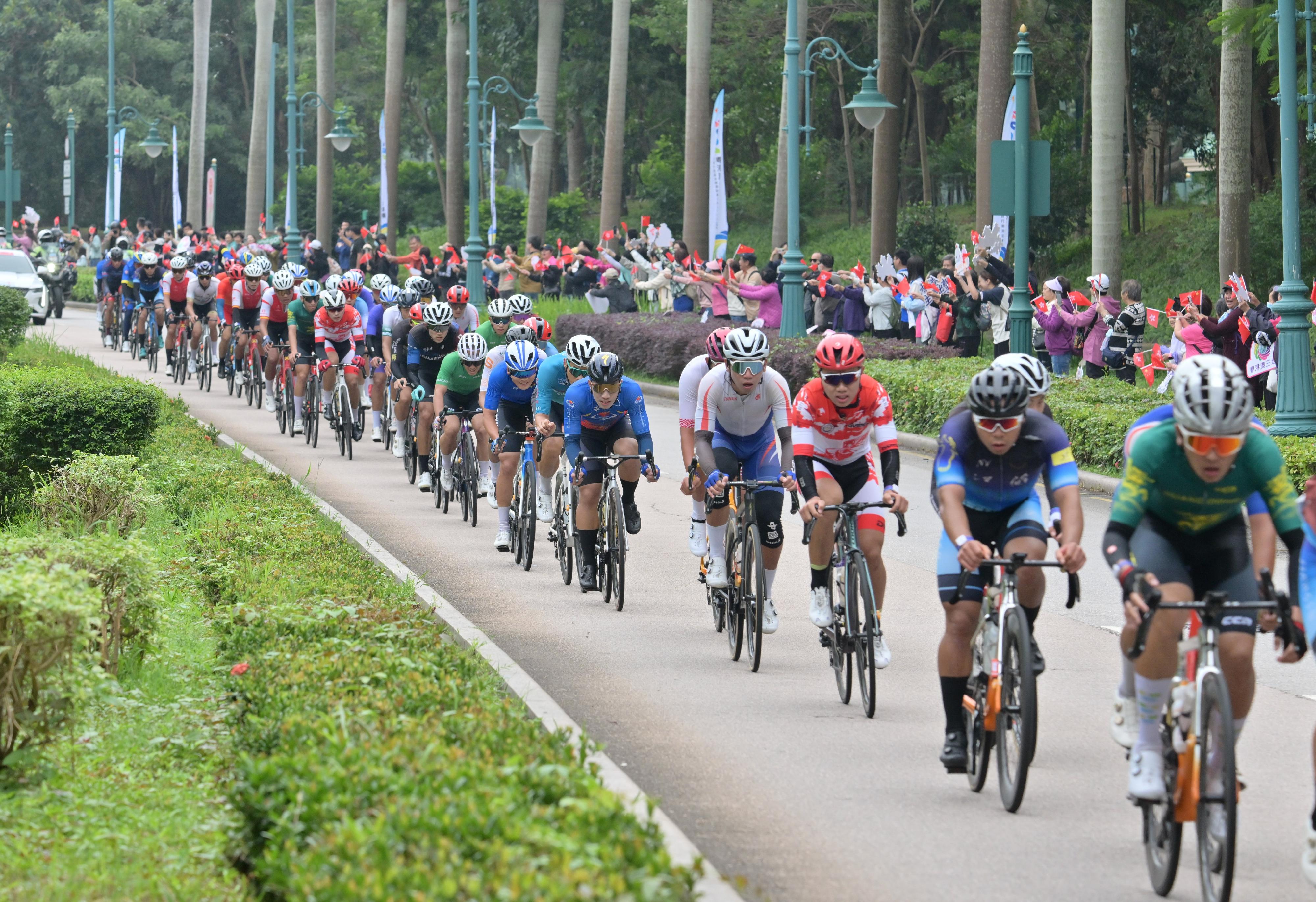 The 2024 Guangdong-Hong Kong-Macao Road Cycling Race and the 15th National Games road cycling test event was held today (November 24) in Zhuhai, Hong Kong and Macao's urban roads and the Hong Kong-Zhuhai-Macao Bridge. Photo shows road racers competing at the race route near the Hong Kong Disneyland Resort and members of the public cheering for the racers at the roadside.