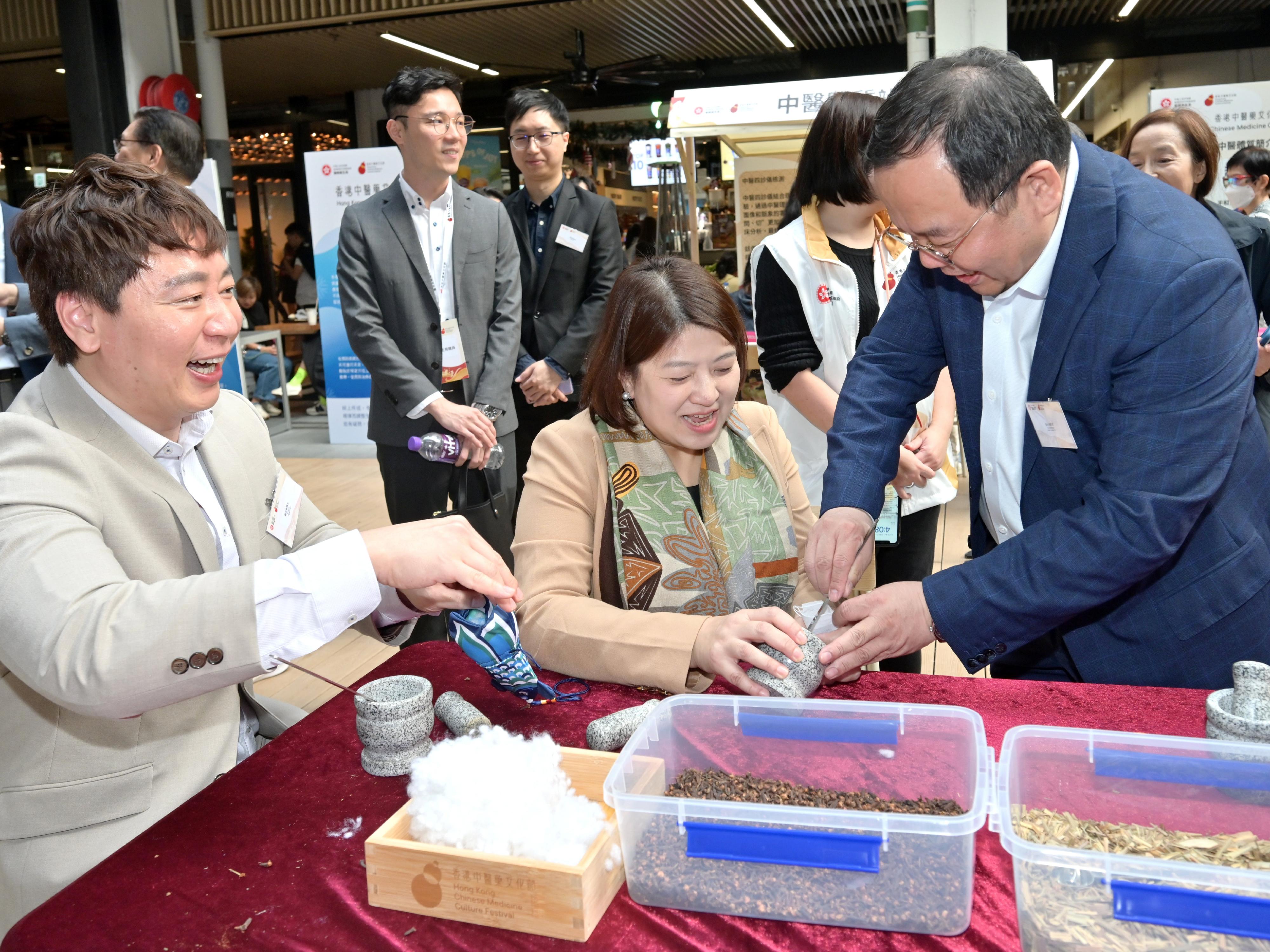 首届「香港中医药文化节」启动活动今日（十二月七日）起一连两日在中环街巿举行。图示署理医务卫生局局长李夏茵医生（中）和中医药发展专员钟志豪博士（左一）参与香包制作。

