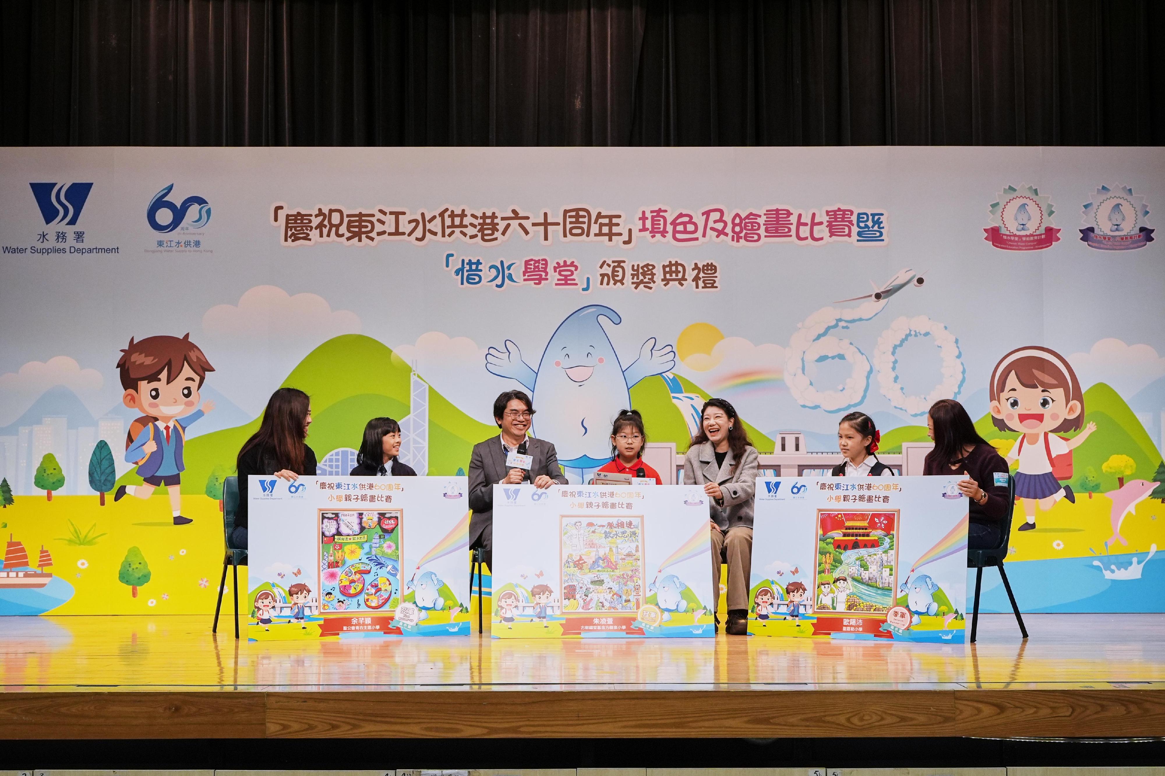 The Water Supplies Department today (December 18) held the Celebration of the 60th Anniversary of Dongjiang Water Supply to Hong Kong Colouring and Drawing Competitions and Cherish Water Campus Award Ceremony to commend the schools, teachers and students for their enthusiastic participation in activities celebrating the 60th anniversary of Dongjiang's Water Supply to Hong Kong and efforts in promoting water conservation. Photo shows the primary school parent-child drawing competition award-winning students sharing with the Director of Water Supplies, Mr Roger Wong (third left), how they express Hong Kong’s strong blood ties with the country in their artworks. 