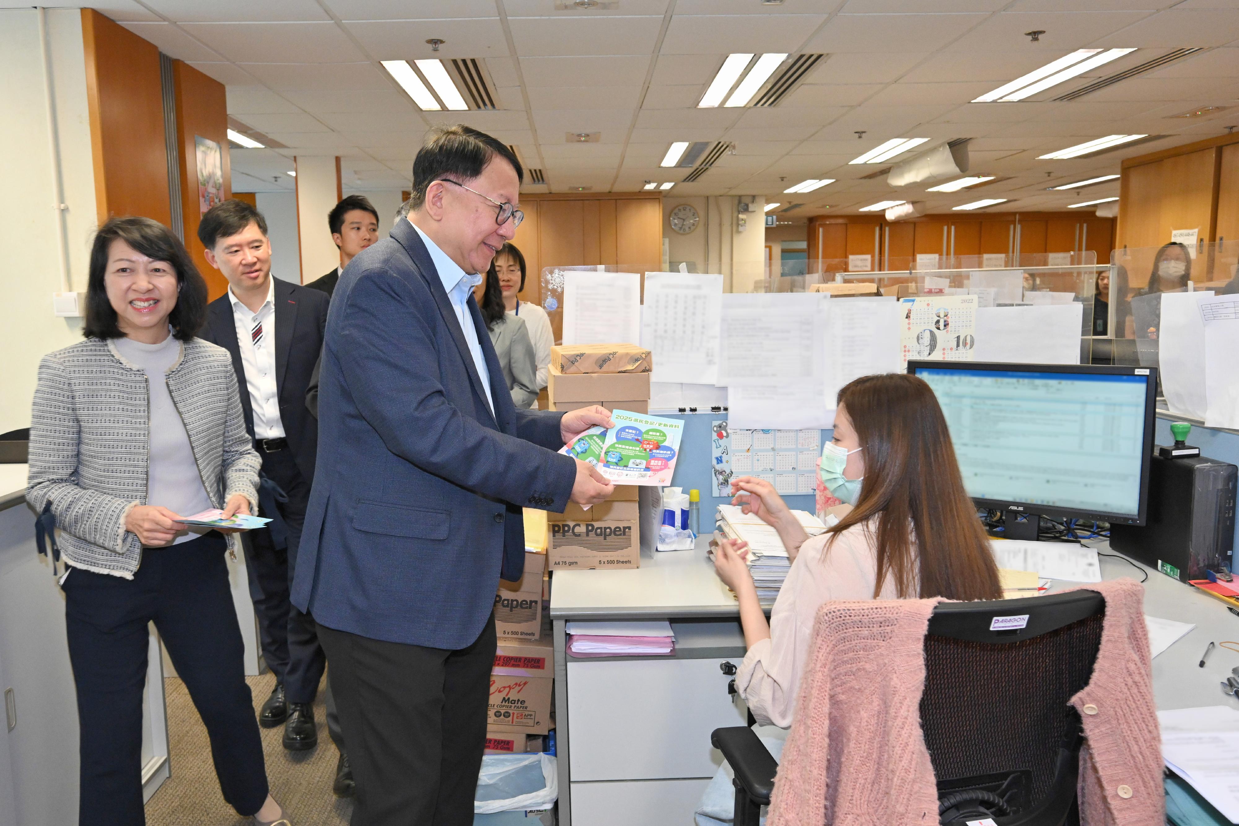 政務司司長陳國基今日（五月十三日）聯同四個公務員中央評議會的代表，一起到位於金鐘政府合署的多個樓層，呼籲同事積極登記成為選民，並在今年十二月七日舉行的立法會換屆選舉踴躍投票，履行公民責任。圖示陳國基（右二）在土地註冊處同事的工作間向他們派發宣傳單張，呼籲同事積極登記成為選民。旁為署理政制及內地事務局局長胡健民（左二）和土地註冊處處長譚惠儀（左一）。